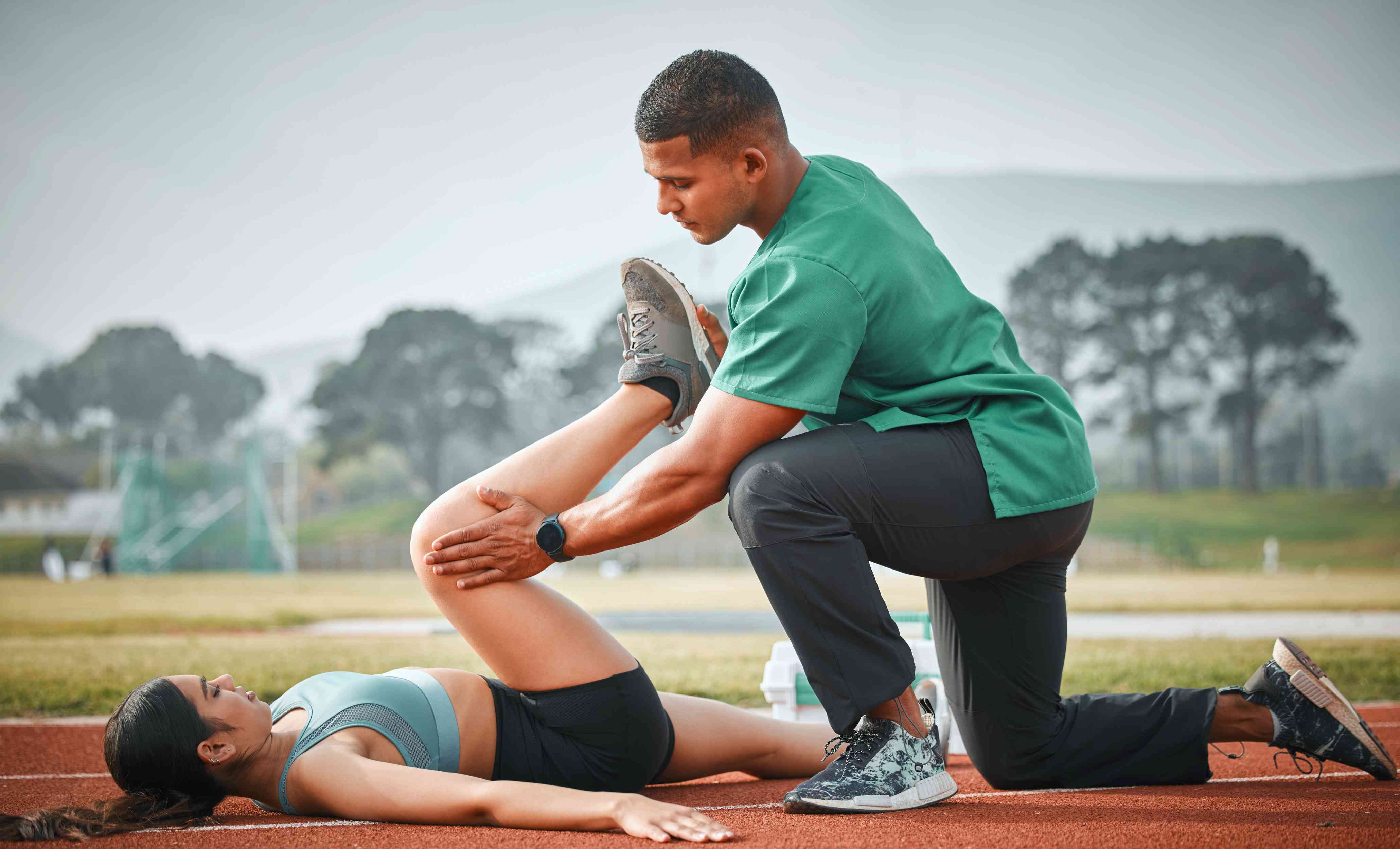 Physical therapist stretching a woman’s leg on a sports track
