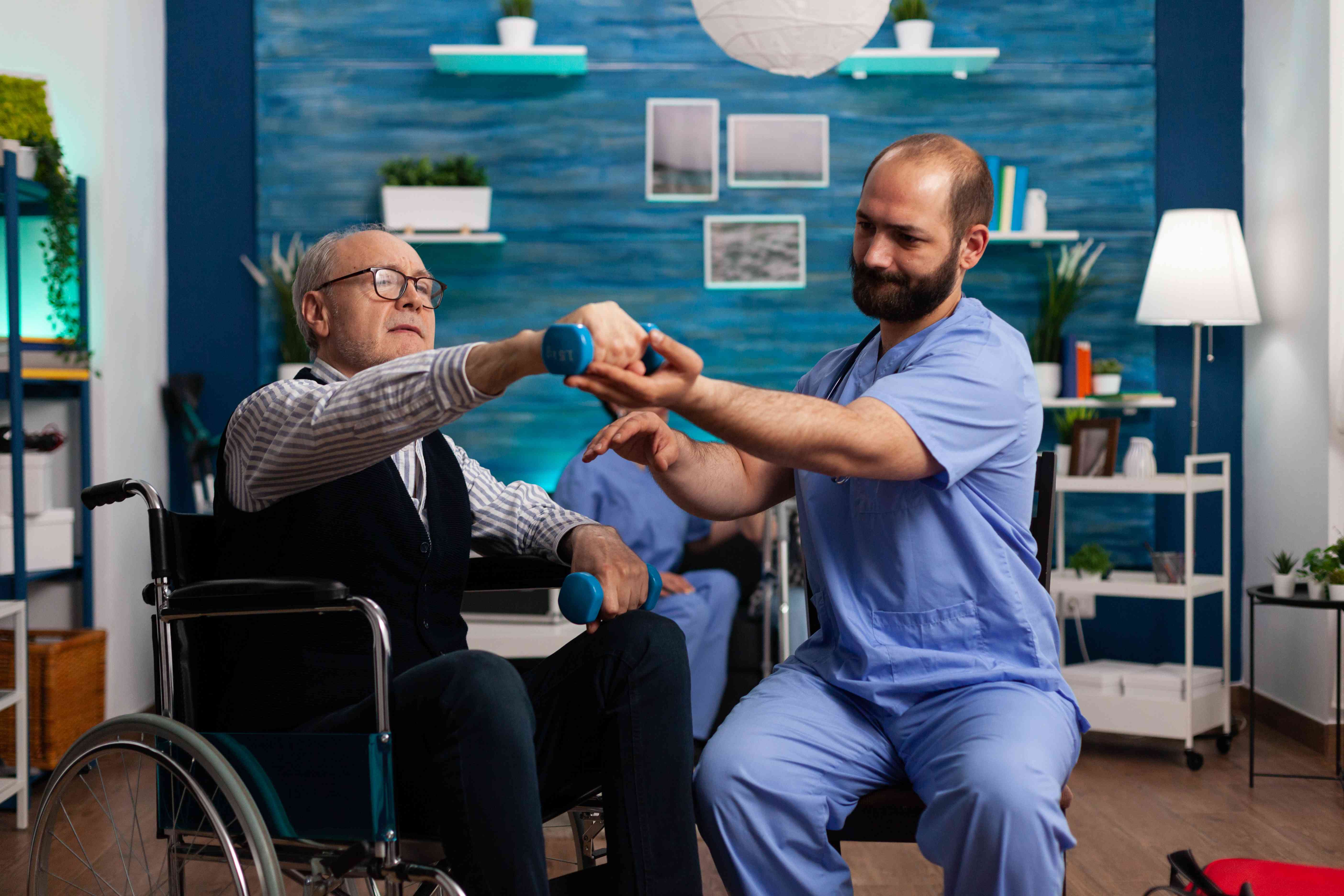 Physiotherapist assisting an elderly man in a wheelchair with arm exercises using dumbbells