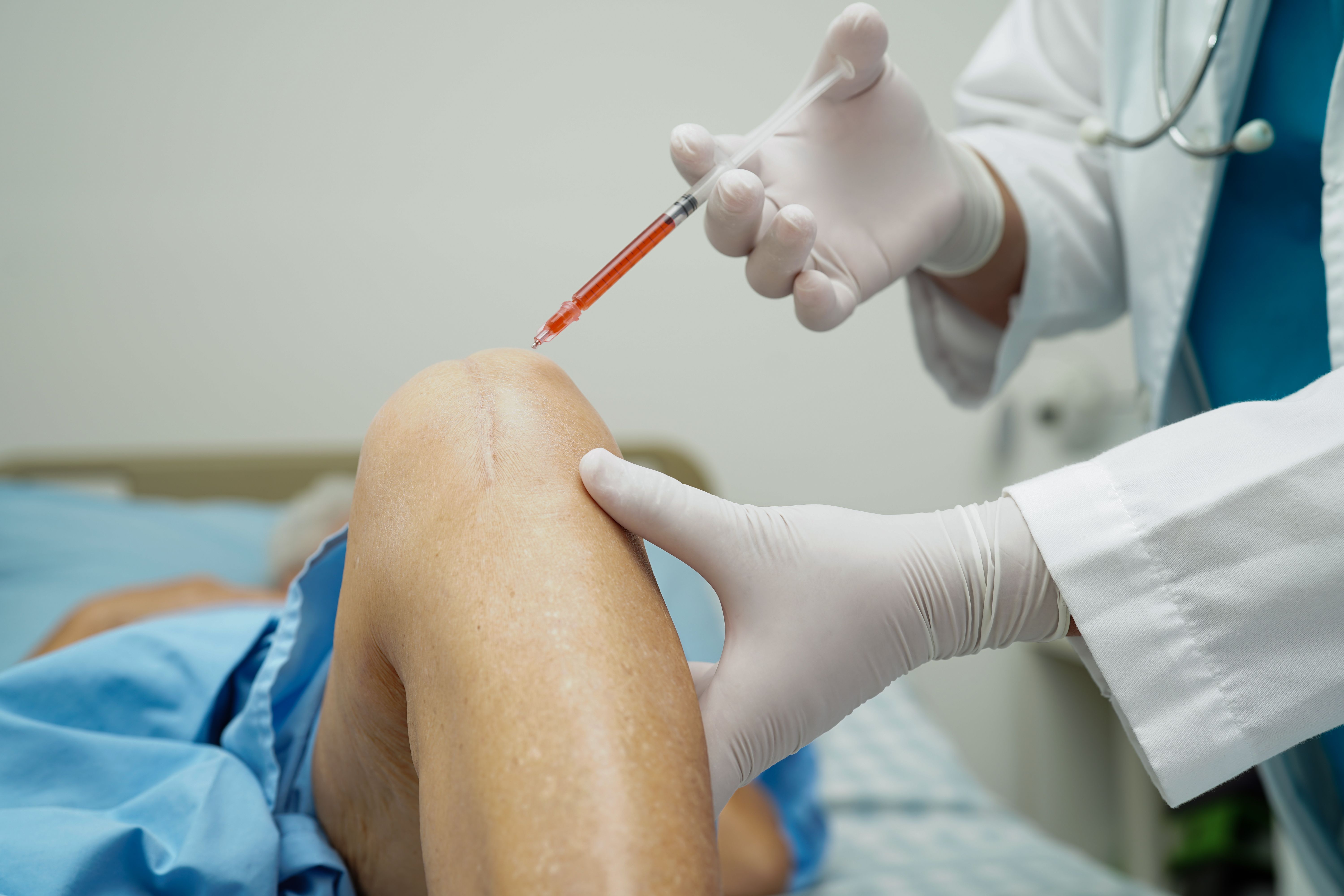 Doctor injecting PRP (Platelet-Rich Plasma) into a senior woman's knee.
