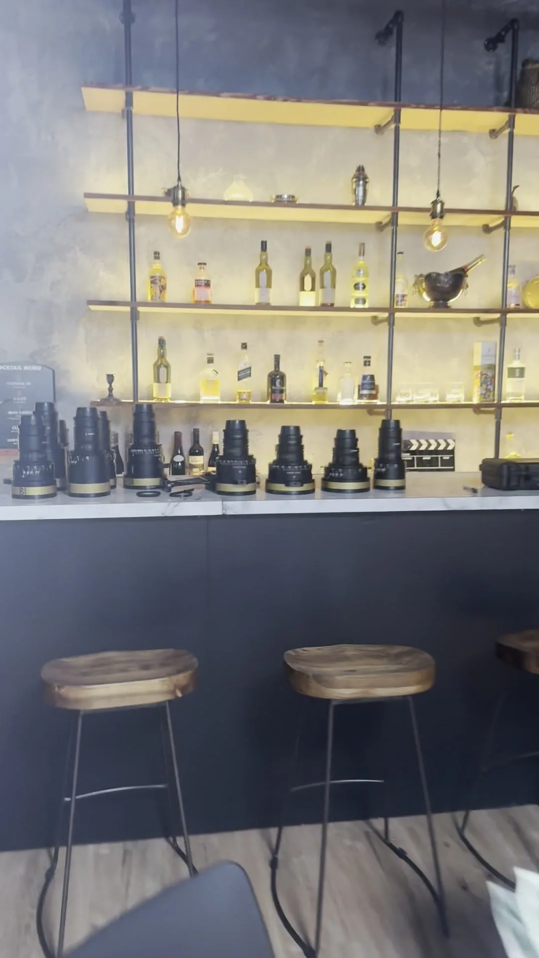 A row of Hawk cinema lenses lined up on a marble bar in front of lit bottle shelves at Hawk London in Stratford