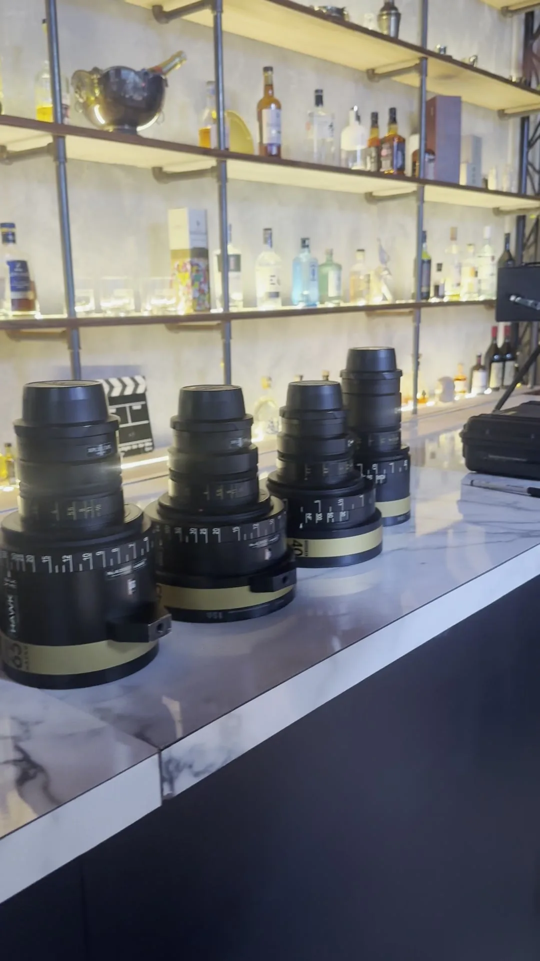 Close-up of a row of cinema prime lenses with gold focal-length bands standing on a marble bar at Hawk London