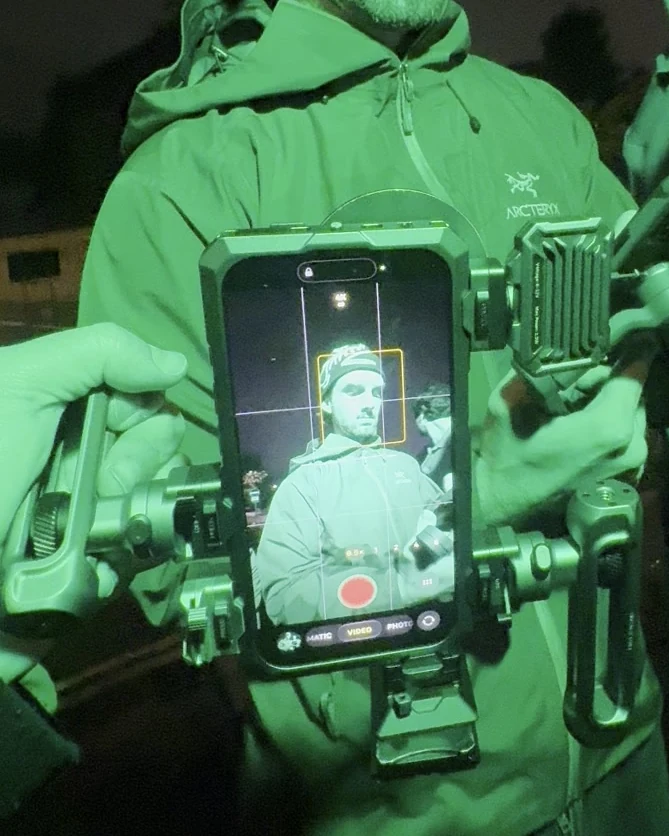 Crew member holding the iPhone 18 Pro cage rig with a cooling fan module while another checks the framing