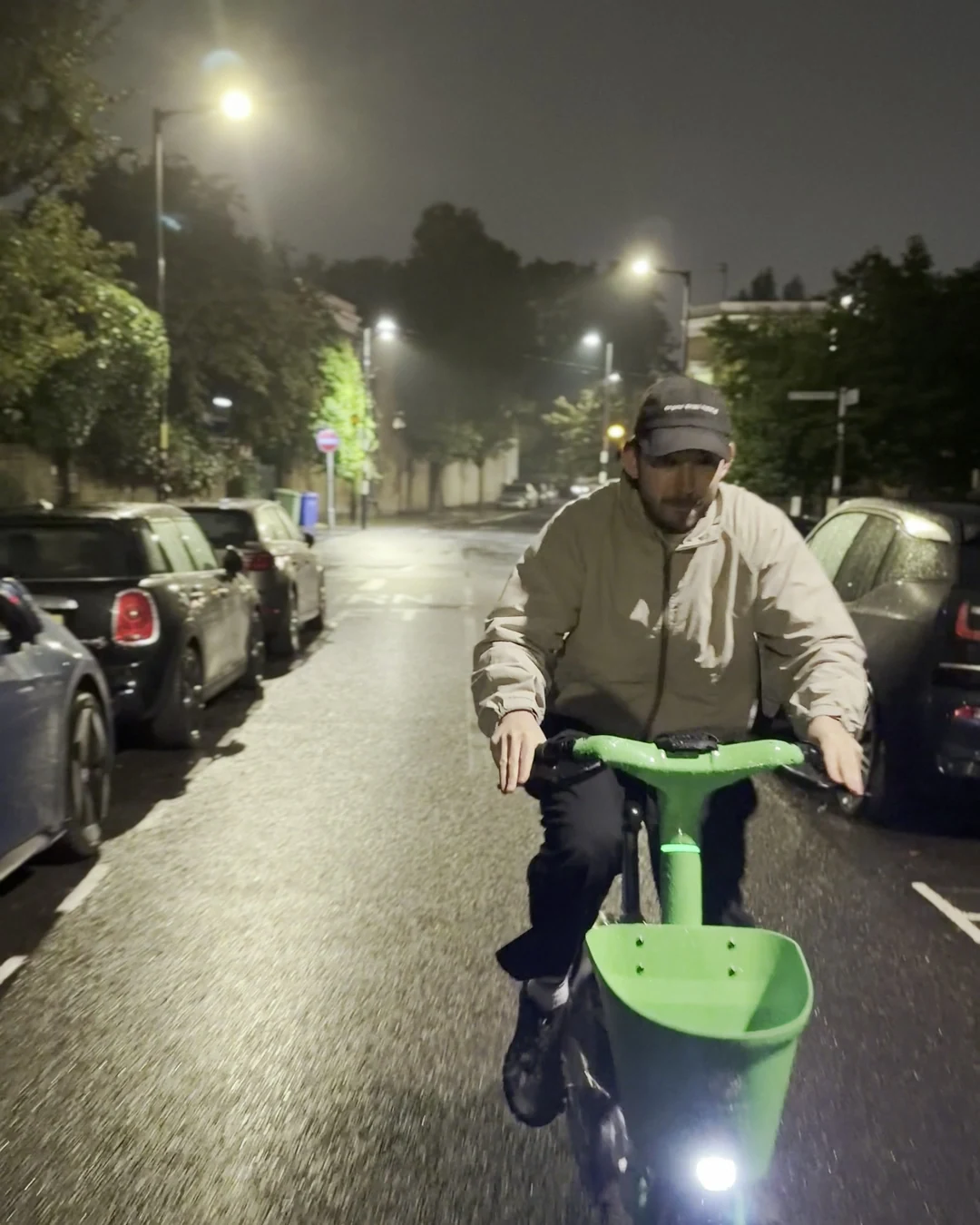 Rider on a Lime bike coming straight at the camera down a wet residential street lit by sodium street lights