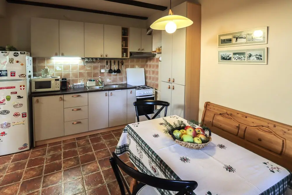 Kitchen with cream cabinets, terracotta floor tiles, and a small dining table set with a bowl of fruit under a yellow pendant lamp