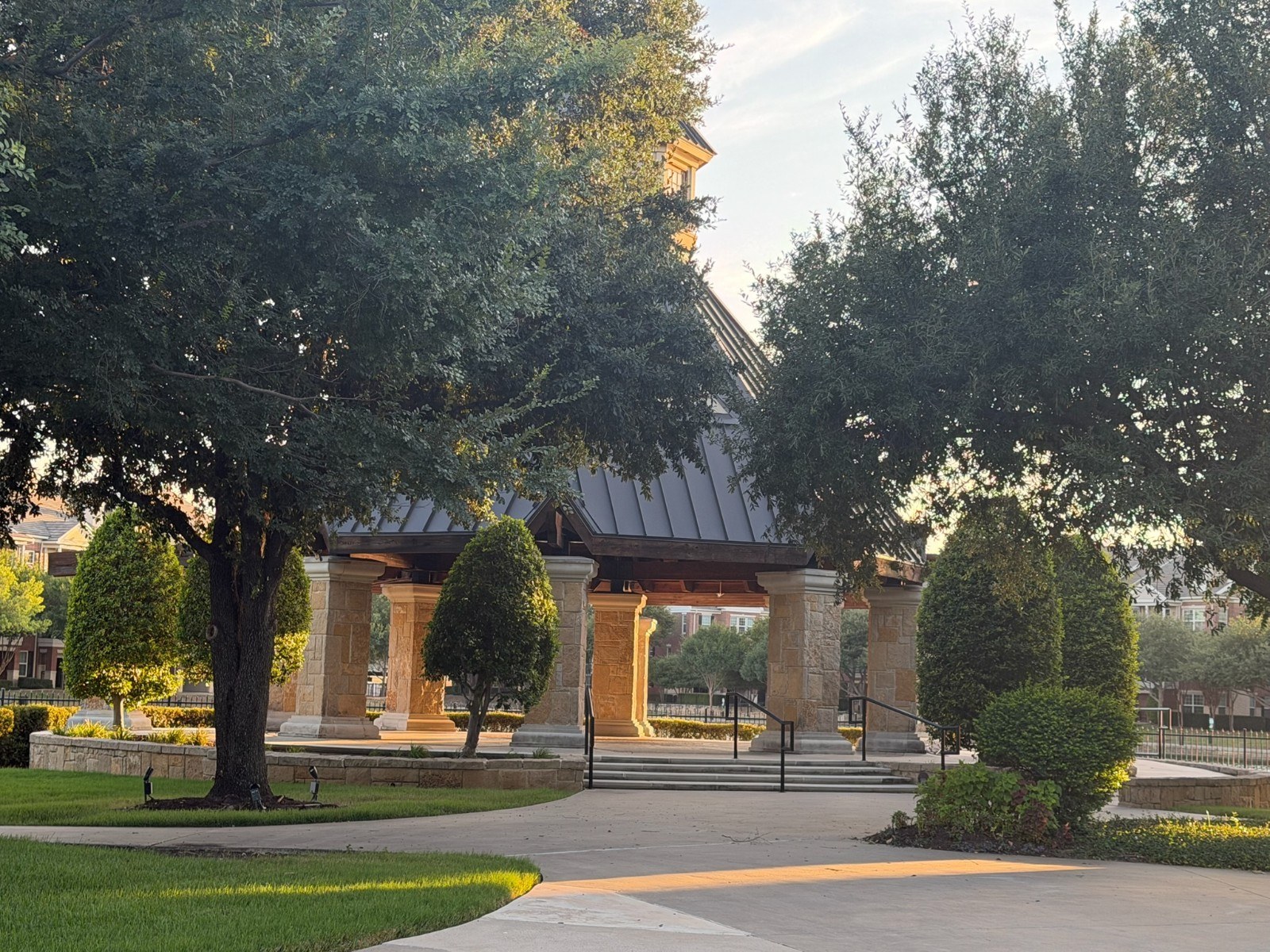 Twilight residential street with warm exterior lights, mature trees, and a glimpse of water