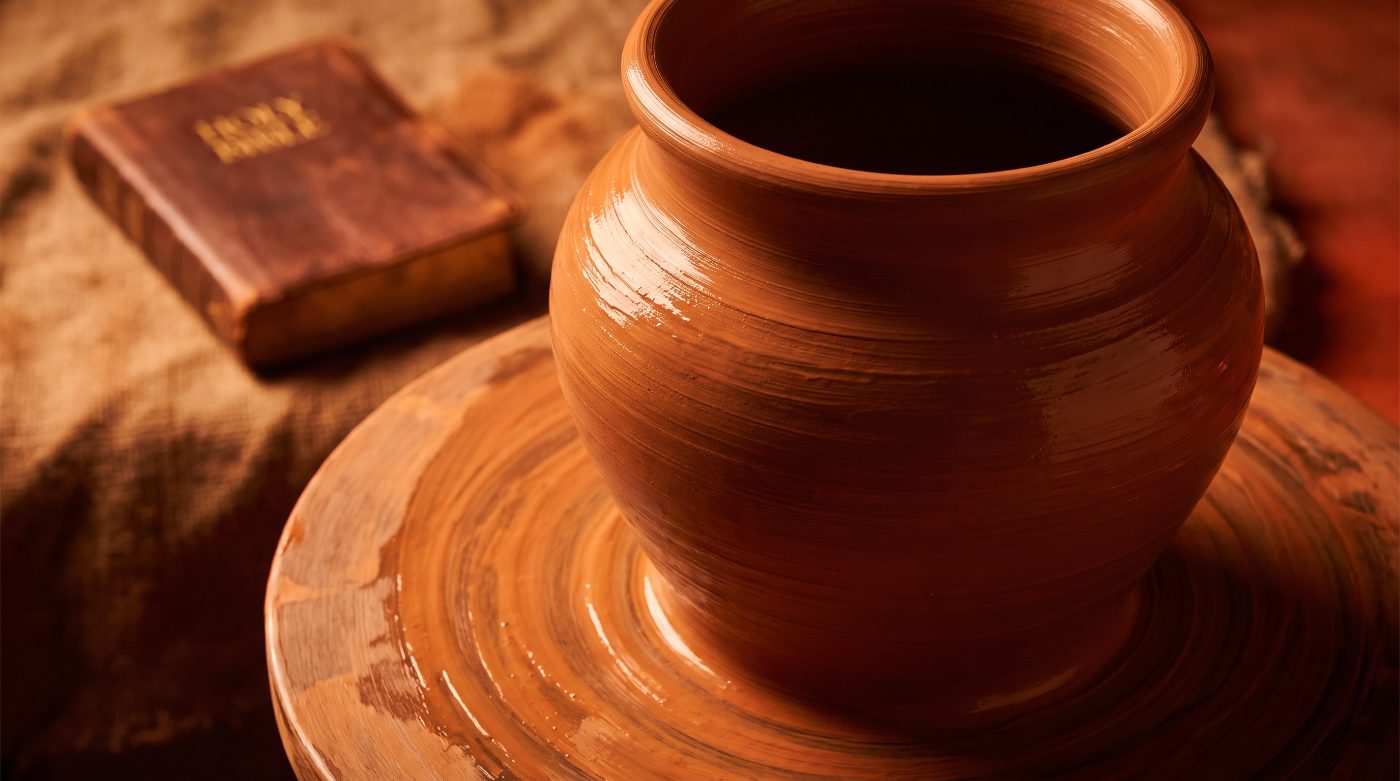 A partially shaped clay vessel on a potter's wheel in saturated warm light