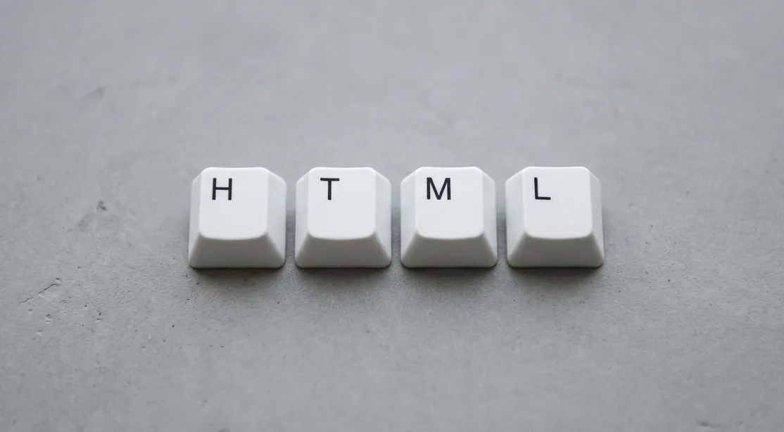 Teclas brancas formando a palavra HTML sobre fundo cinza liso, simbolizando linguagem de marcação usada na web.