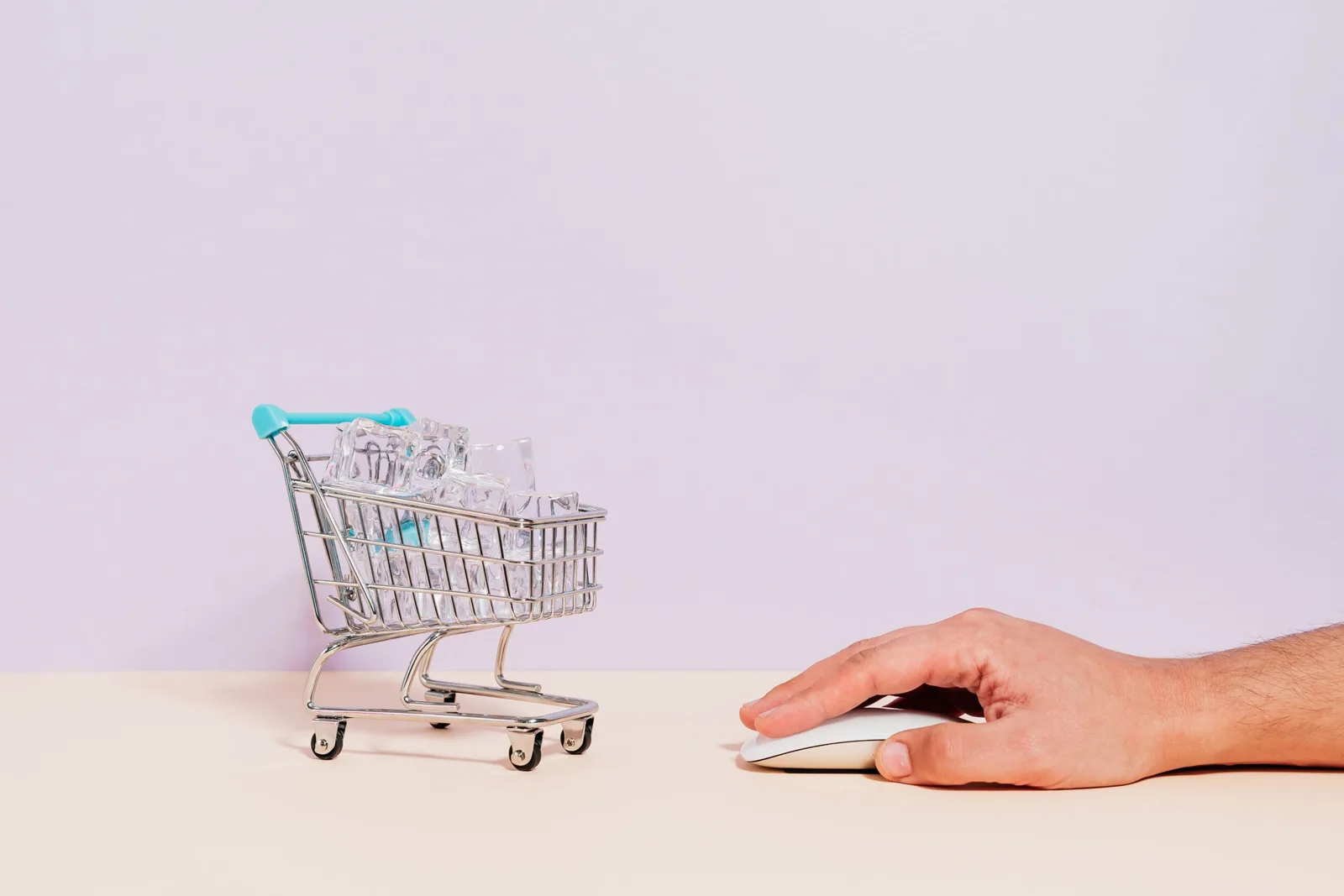 Mão masculina usando mouse de computador ao lado de mini carrinho de compras com gelo, representando a inovação congelada em uma plataforma de e-commerce legada.