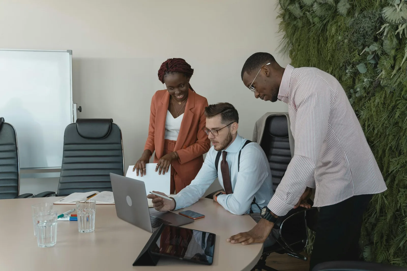 Um grupo diversificado de três profissionais de negócios colaborando ao redor de uma mesa com notebook aberto e tablet, representando a governança humana necessária para implementar sistemas de Inteligência Artificial na empresa.