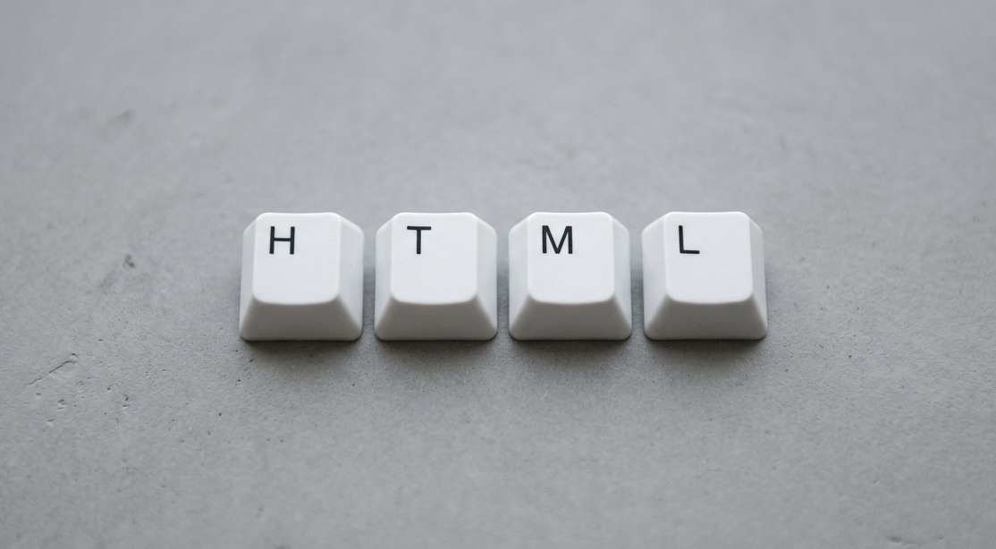 Teclas brancas formando a palavra HTML sobre fundo cinza liso, simbolizando linguagem de marcação usada na web.