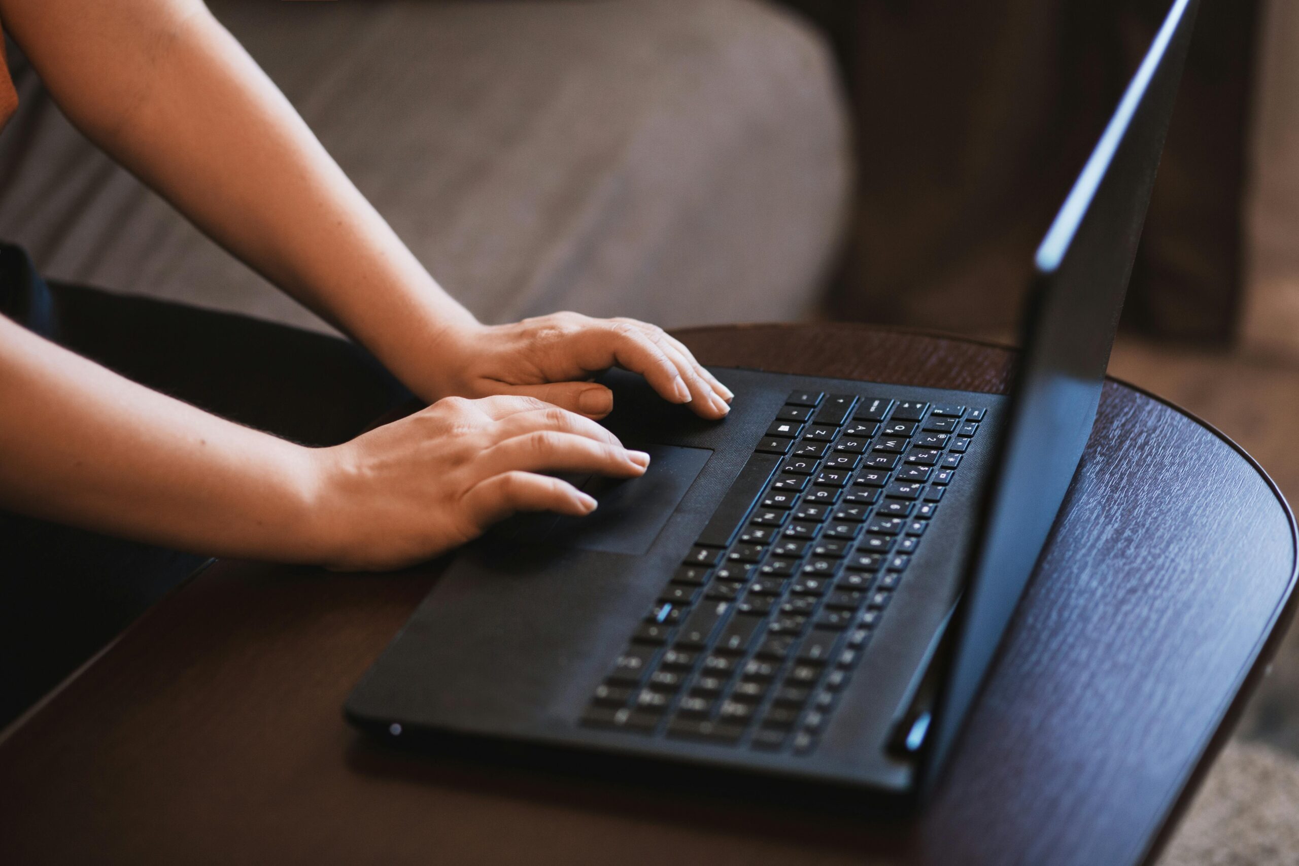 Mãos de uma pessoa digitando em um notebook preto sobre uma mesa de madeira, acessando ferramentas de inteligência artificial online.