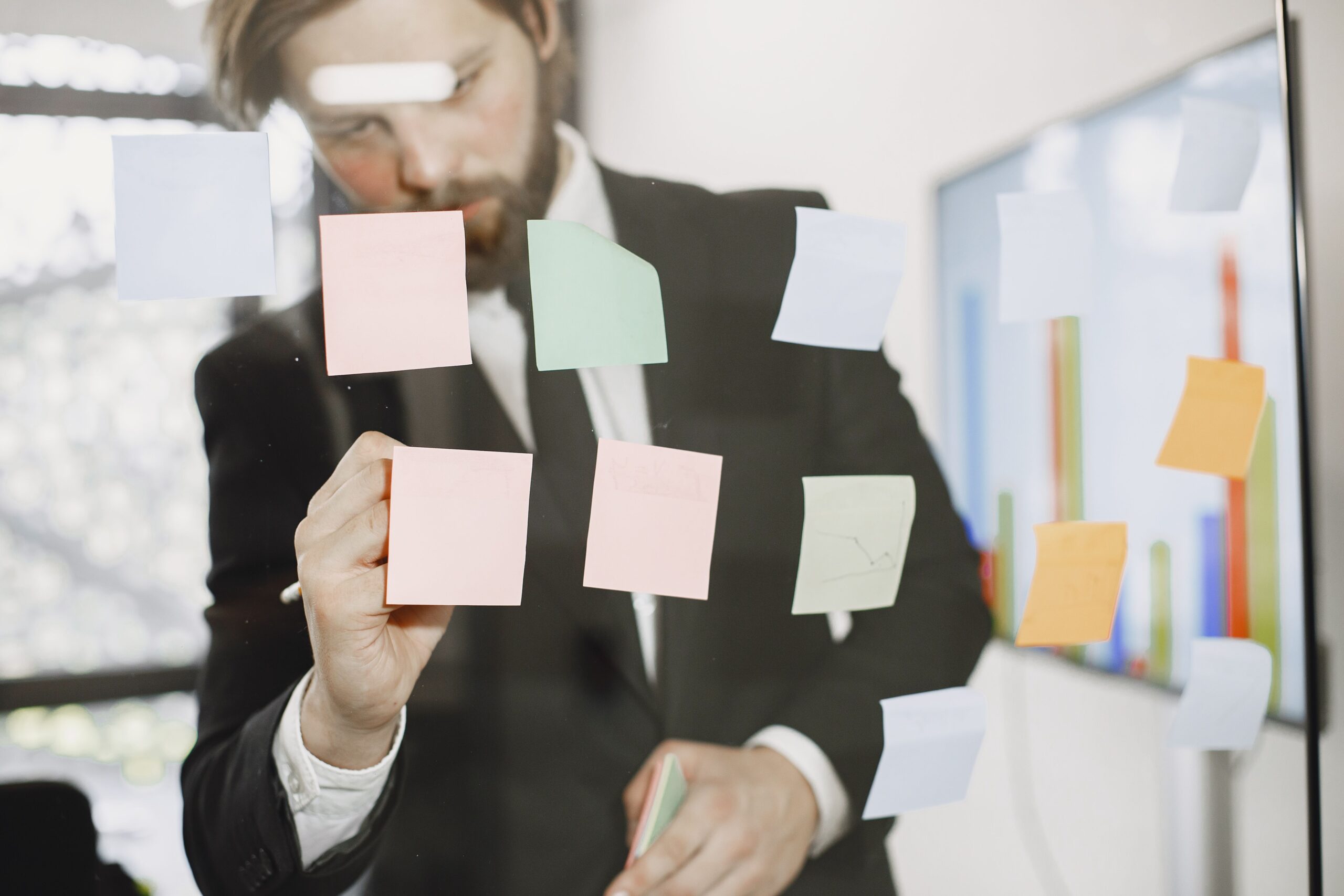 Profissional em escritório organizando notas adesivas coloridas em um painel de vidro, exercitando o pensamento crítico e criativo contra os impactos da IA no mercado de trabalho.