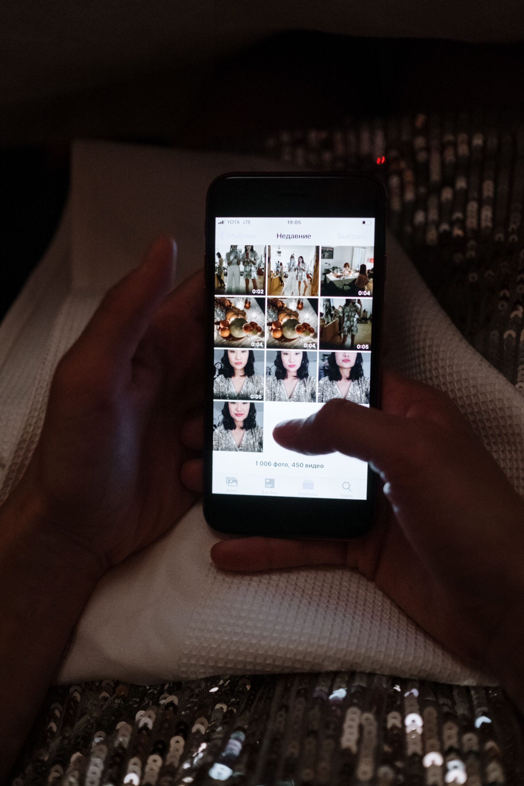 Duas mãos segurando um celular em ambiente escuro, navegando por uma galeria de fotos pessoais expostas na tela, ilustrando o perigo de rastreamento e a necessidade de segurança digital para proteger imagens contra a IA.