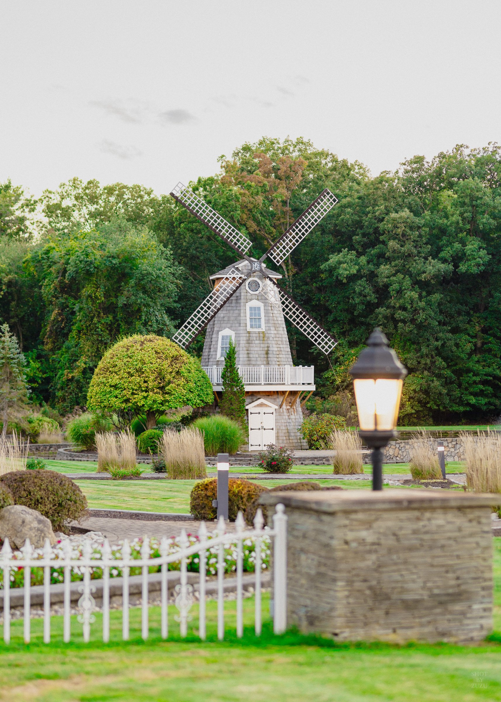 Gray shingled windmill surrounded by gardens and a white picket fence at a wedding venue