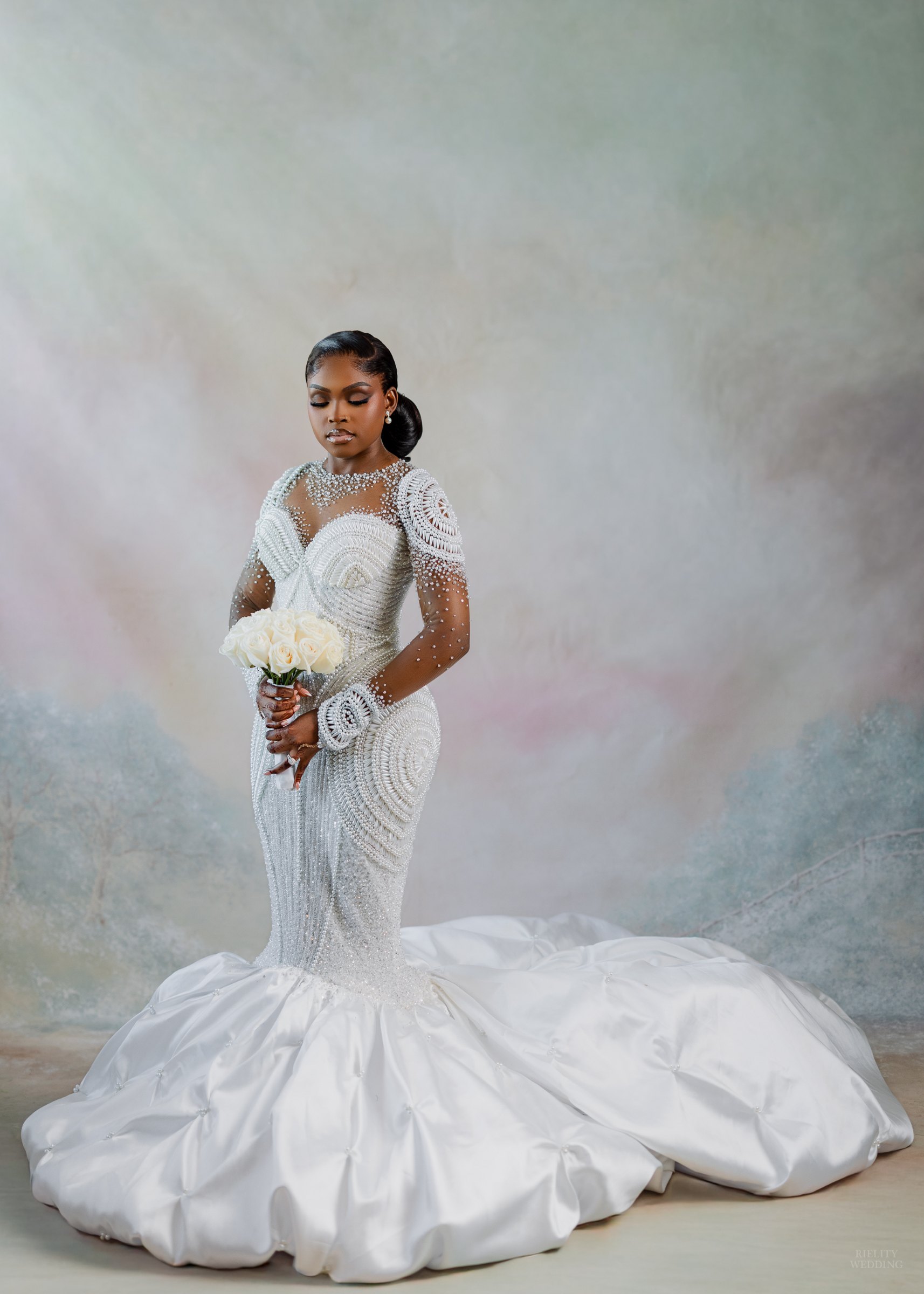 Bride in a beaded mermaid gown holding white roses in front of a painted pastel studio backdrop