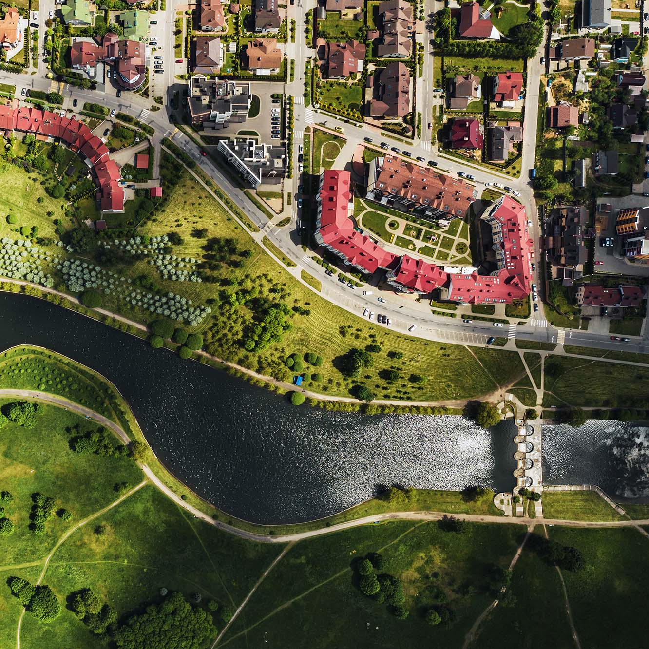 An aerial view of a city with a river, bridge, farmland, and buildings with red roofs.