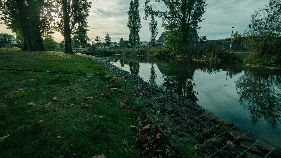 De Stakenbeek in Oldenzaal met een feederhengel boven het water, een stenen oever in gaas en bomen in tegenlicht