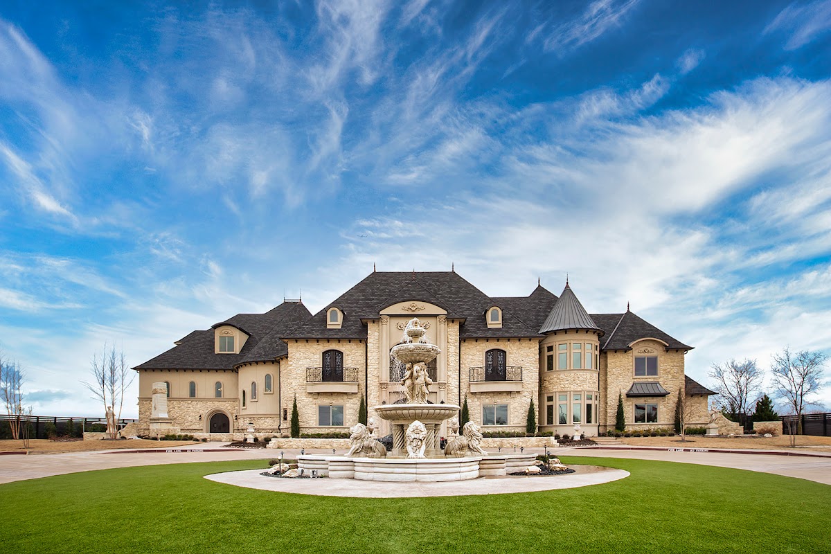 Knotting Hill Place, Little Elm — the turreted château and its formal fountain under a blue sky