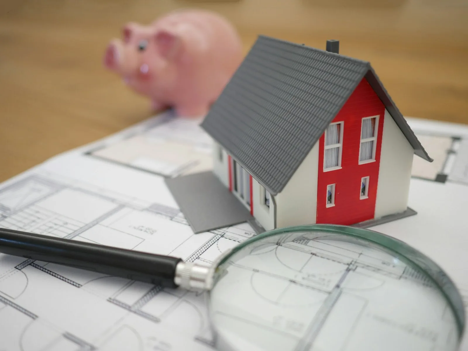 Maqueta de una casa junto a una alcancía y planos, sobre un escritorio