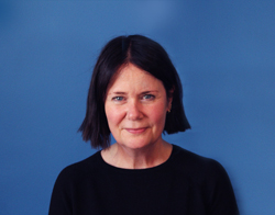 A smiling woman in a black top with red dots on stood in front of a dark blue background