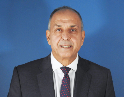 A man smiling in a dark suit and polka dot of dark blue and red dots tie stood in front of a dark blue background