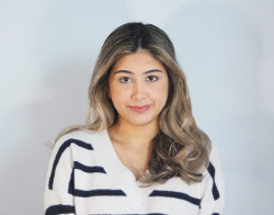 A smiling woman with curly dark hair in a black and white striped jumper stood in front of a light blue background