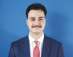 A man smiling man with dark hair and a moustache in a navy blue suit and red tie stood in front of a dark blue background