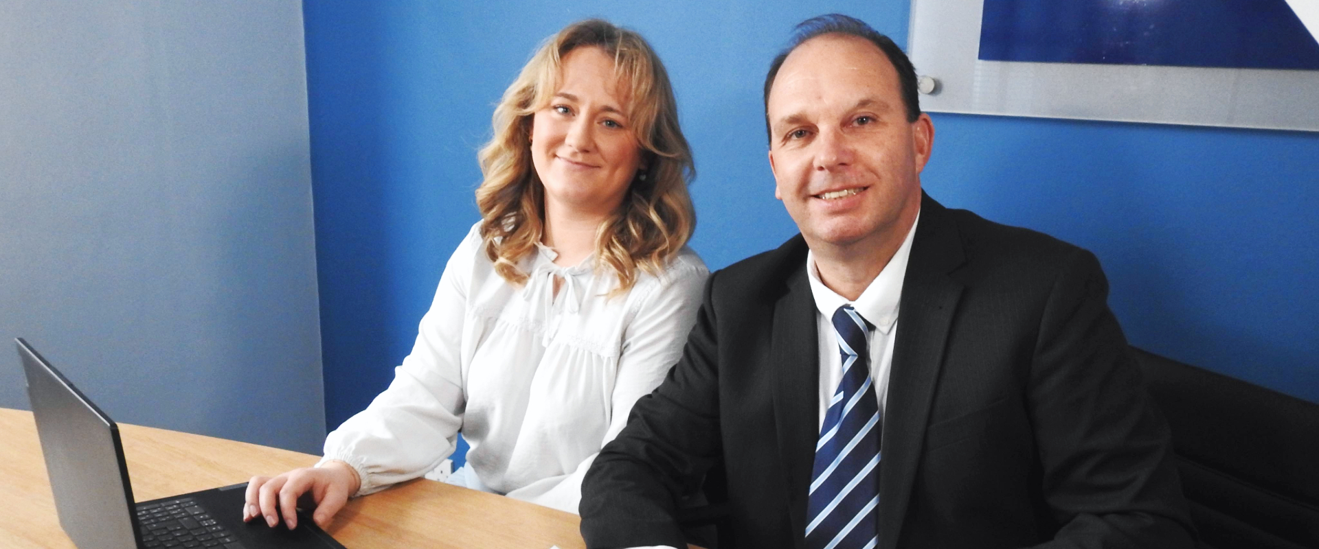 Two advisers in business attire smiling next to a laptop.