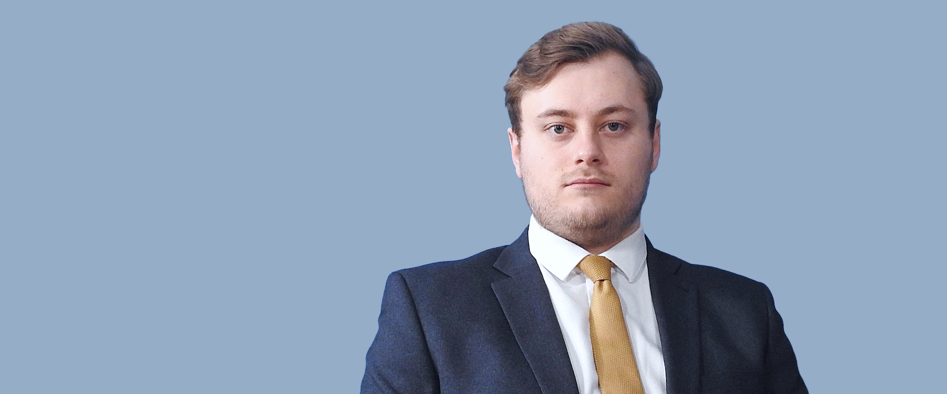 An adviser wearing a blue suit and yellow tie sat in front of a blue background.