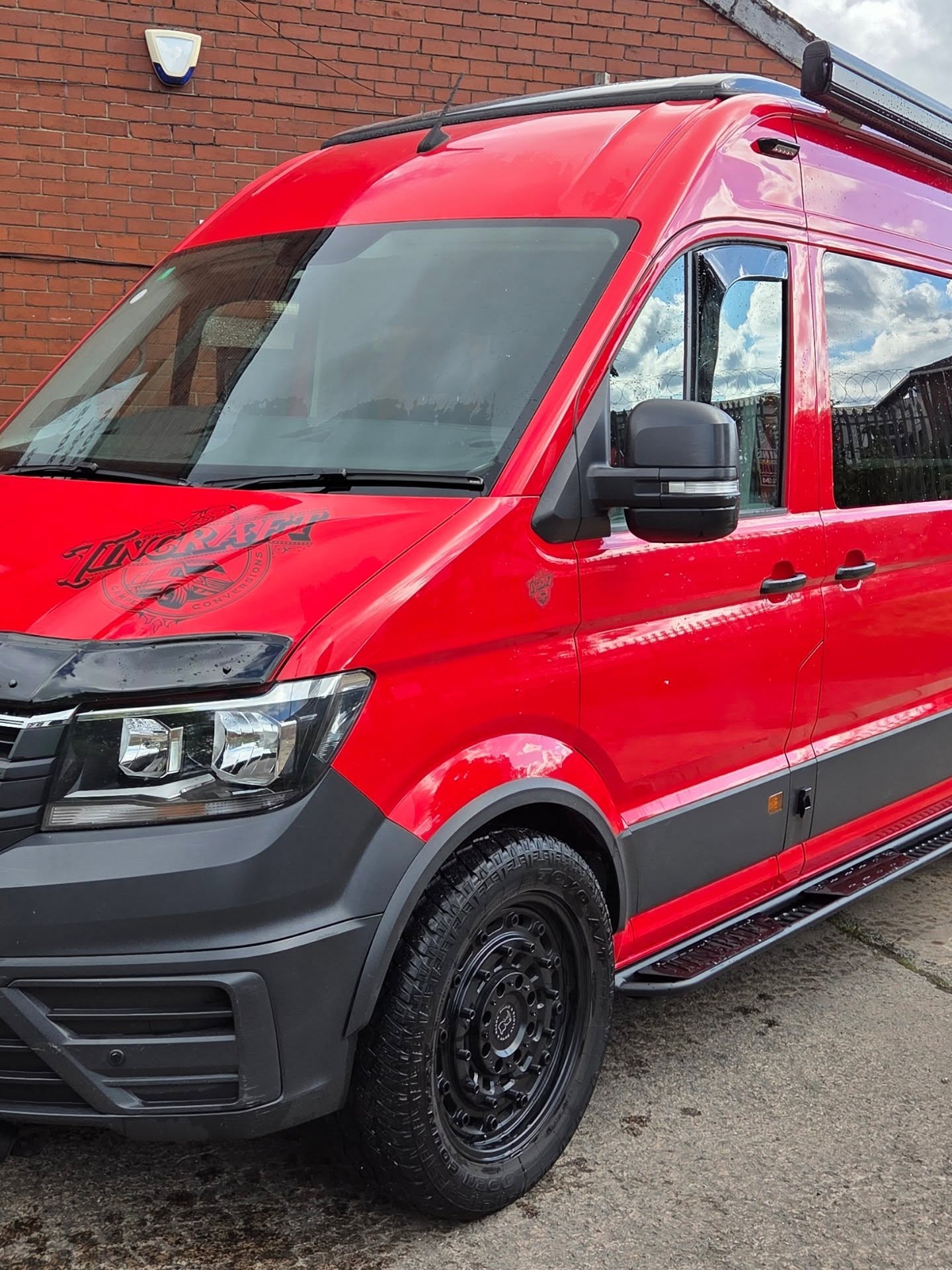 Red VW Crafter overland camper conversion, front three-quarter view with black steel wheels and side steps