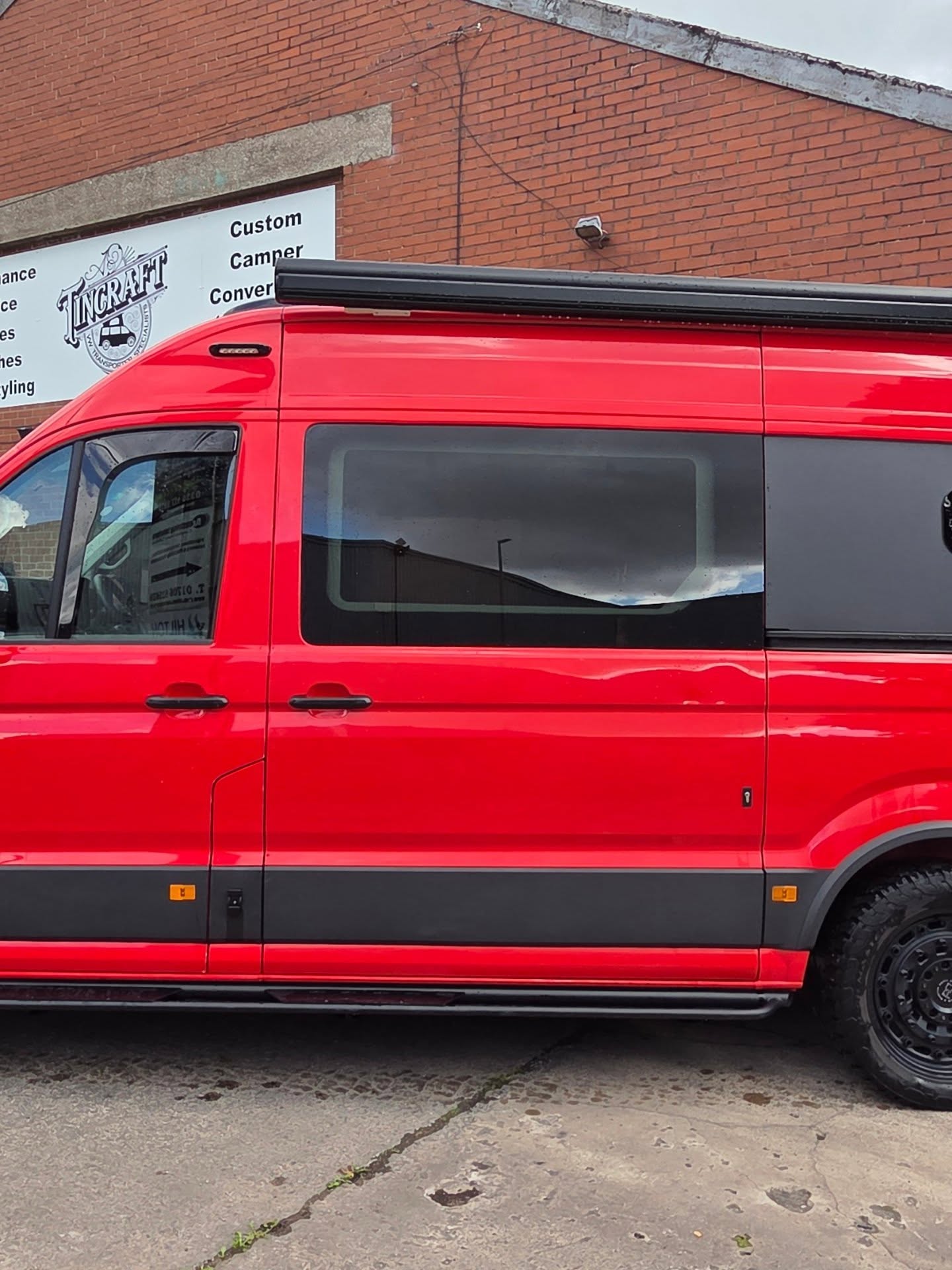 Side profile of a red VW Crafter camper conversion with a roof-mounted awning outside the Tincraft workshop
