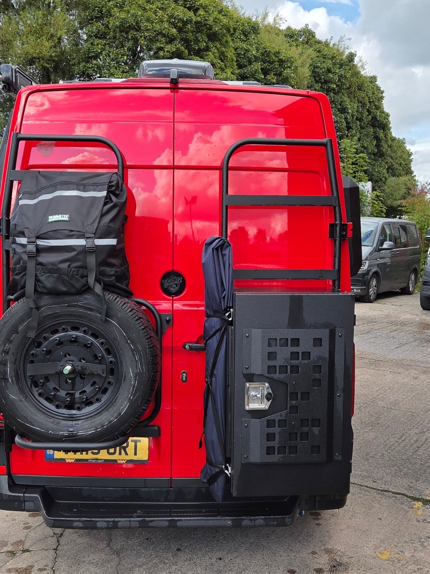 Rear of a red VW Crafter camper with ladder, spare wheel carrier and MOLLE storage panel on the door