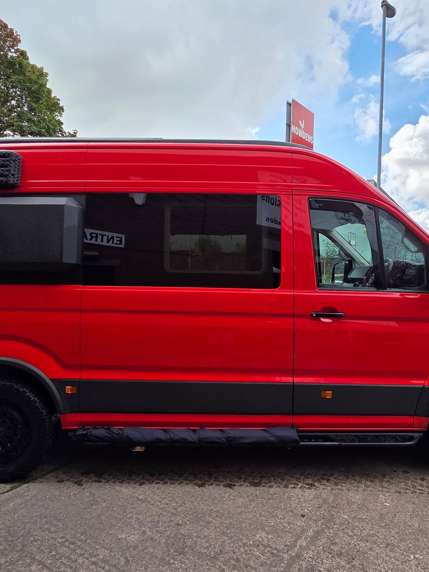 Red VW Crafter overland camper conversion in side profile against a blue sky