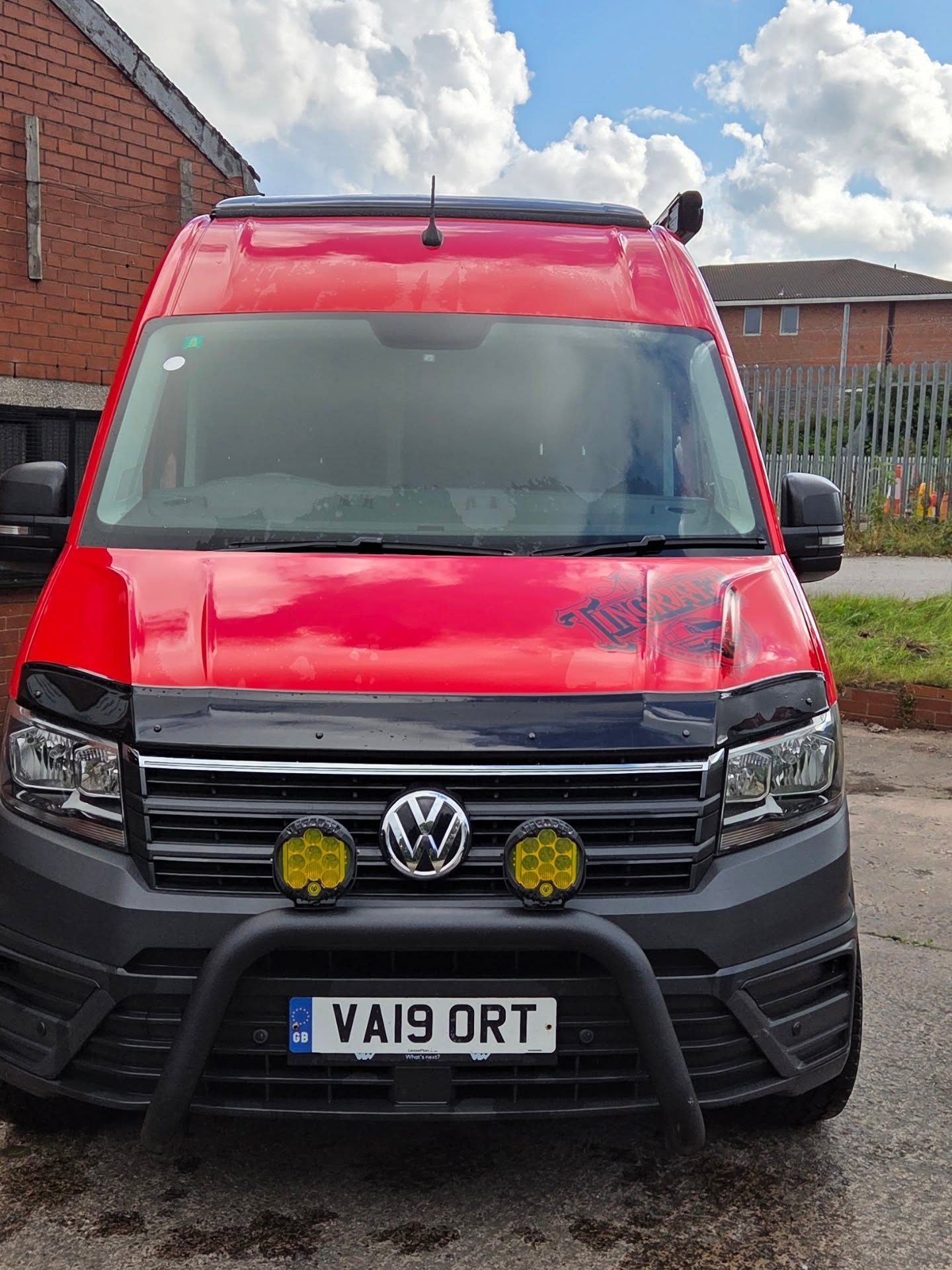 Front of a red VW Crafter camper with a black bull bar and two yellow LED spotlights
