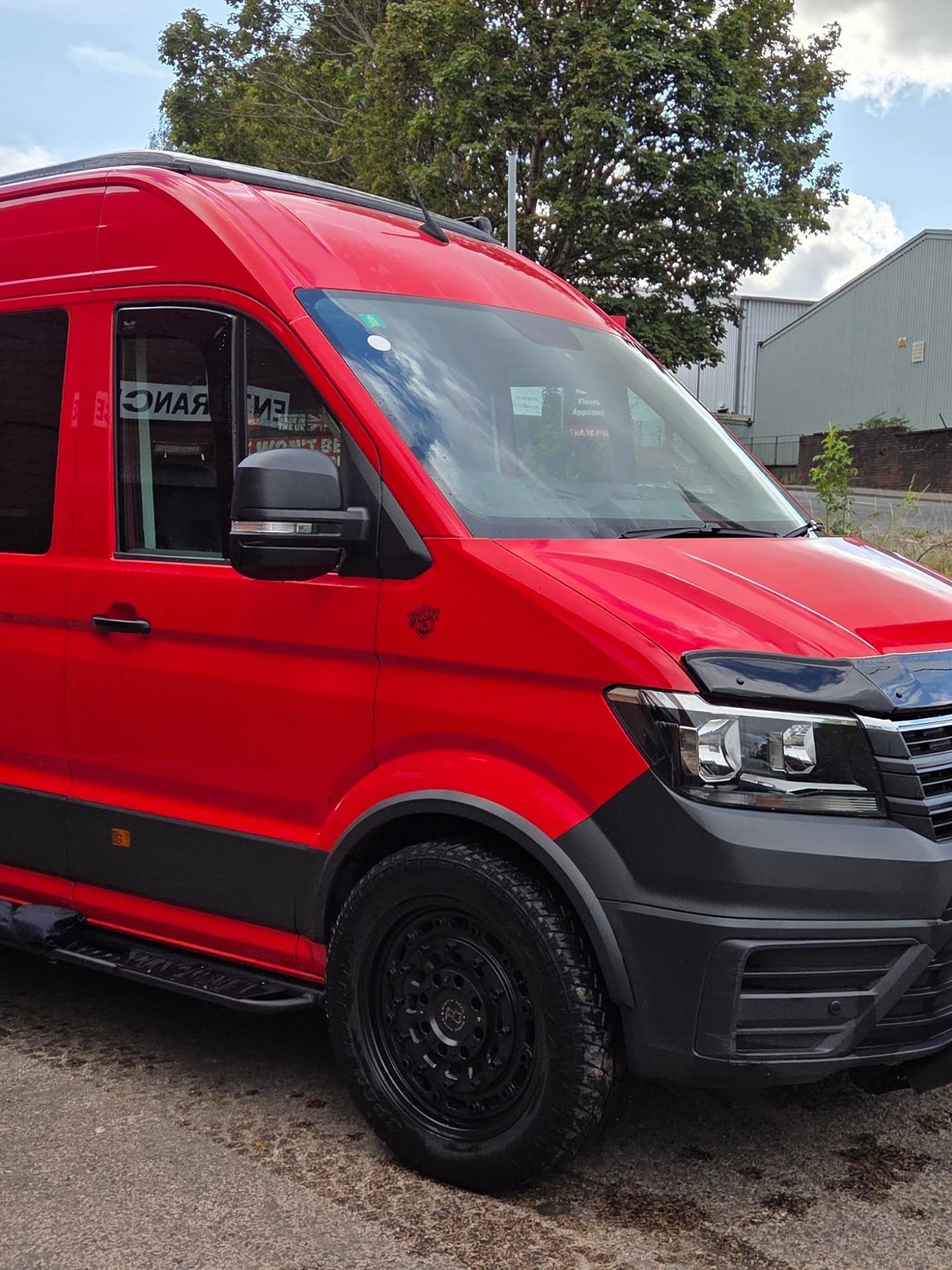 Red VW Crafter camper conversion viewed from the front side, showing black wheel arches and side steps