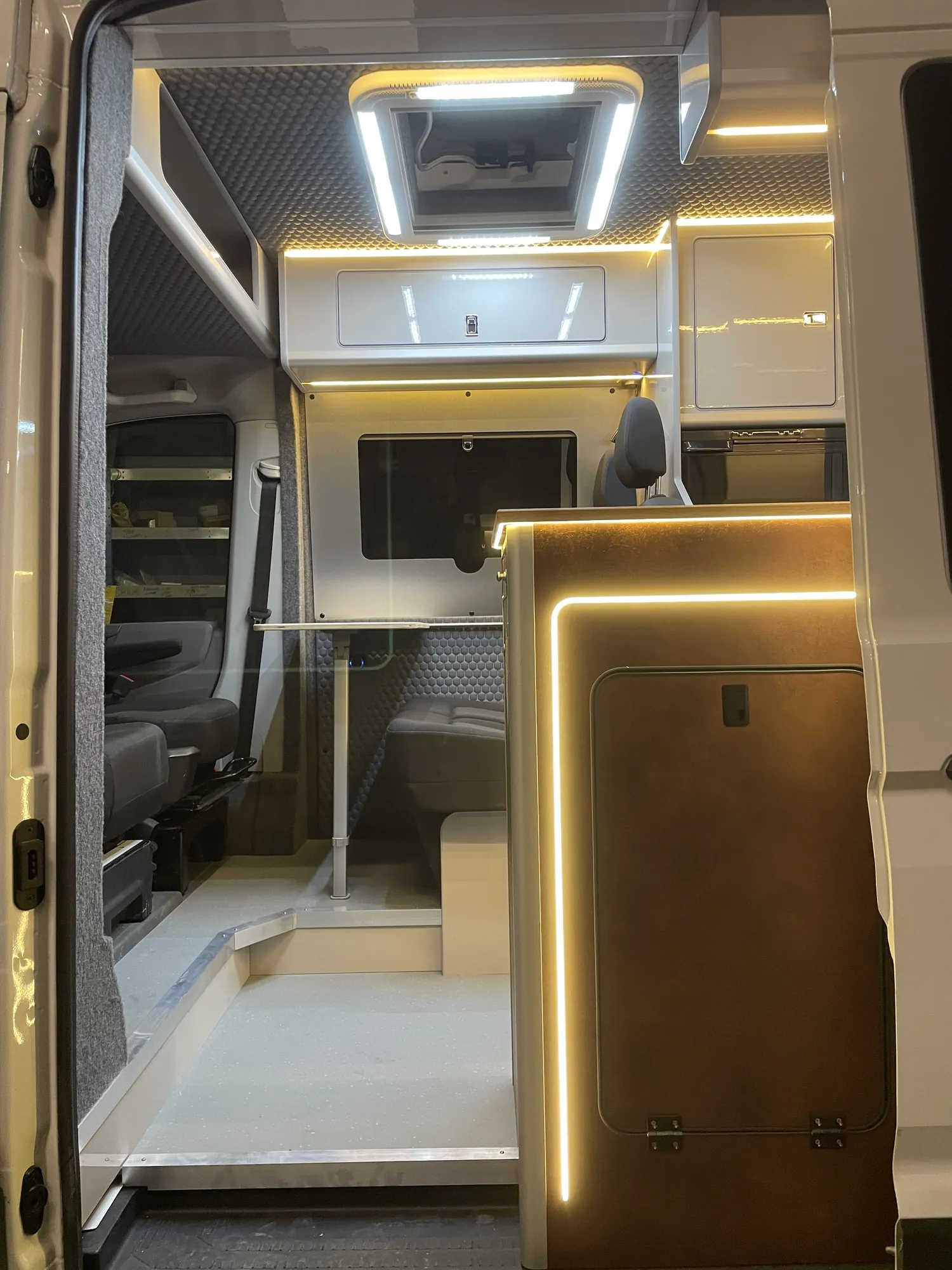 Open side door of a MAN TGE camper, warm LED lighting falling on oak worktops inside