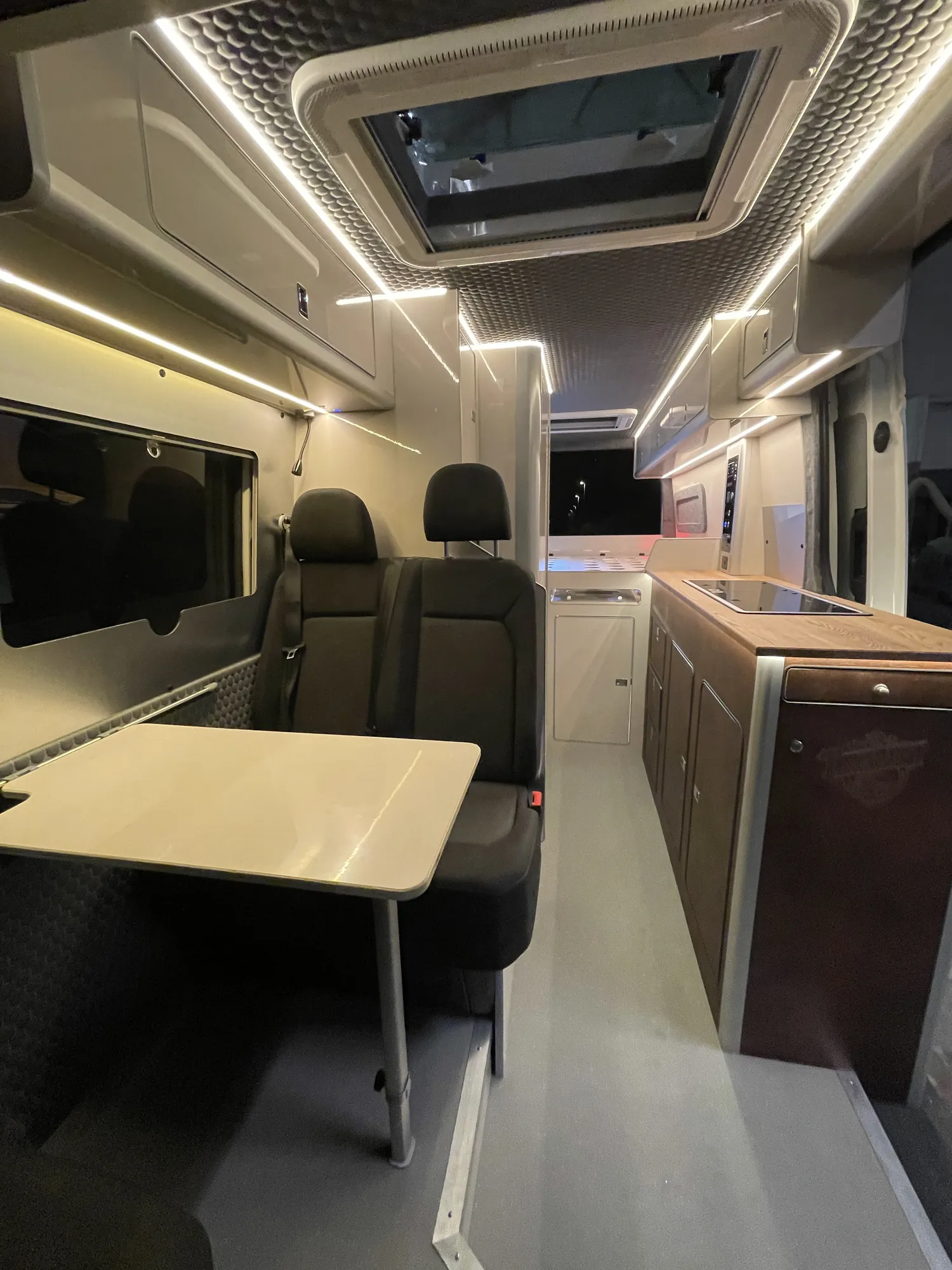 Dinette seating and table under a rooflight in a MAN TGE campervan, LED cove lighting above