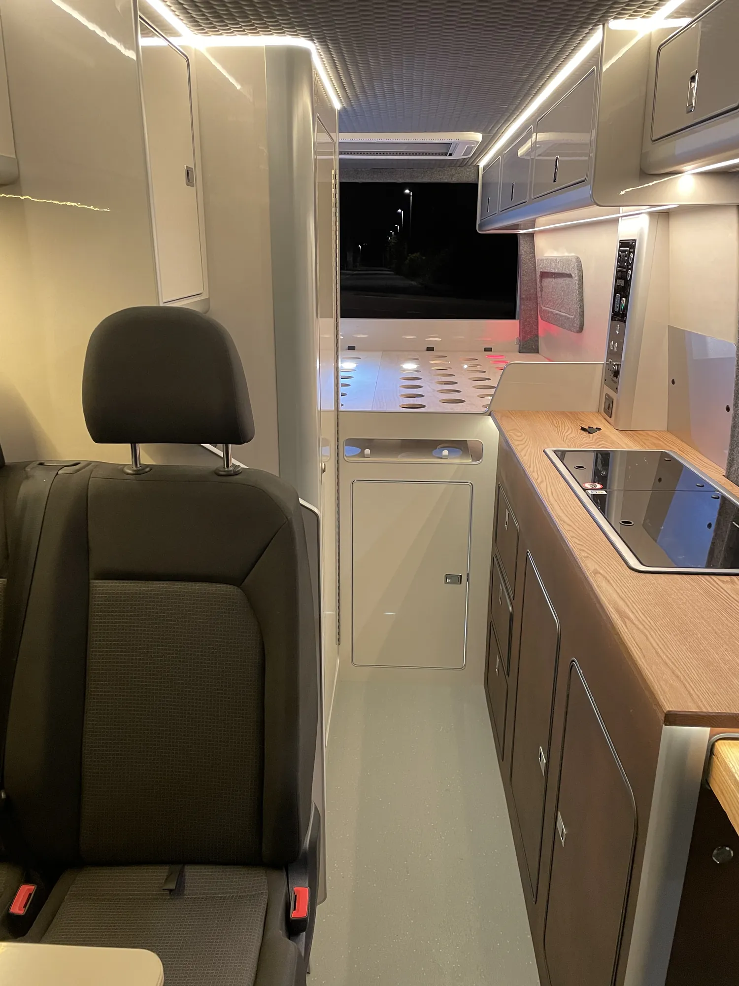 Interior of a MAN TGE camper looking down the van toward the galley and wall-mounted screen