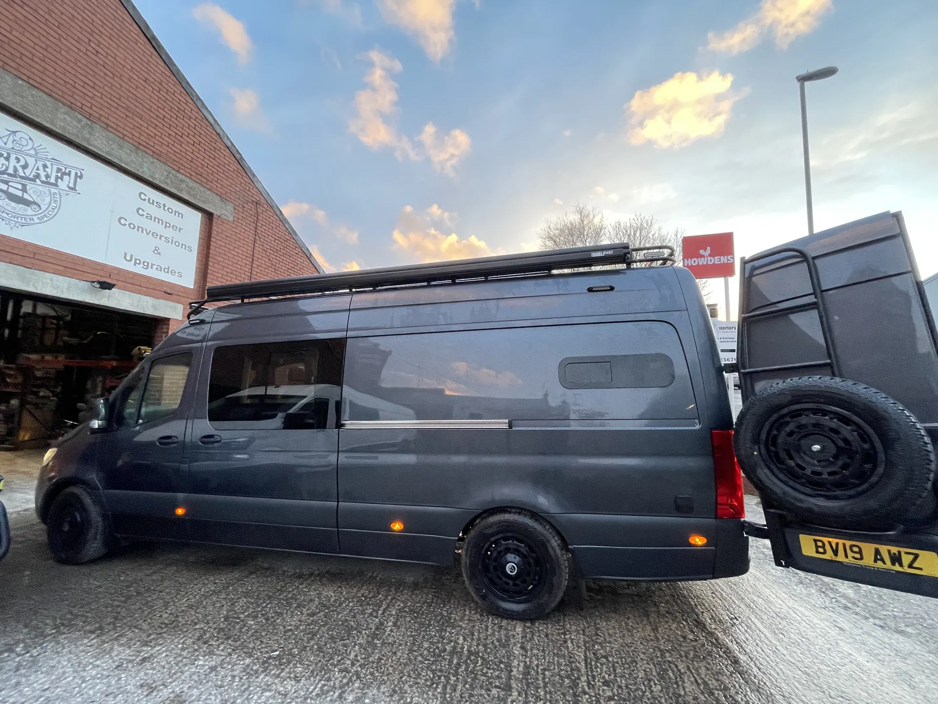 Dark grey Mercedes Sprinter camper conversion in side profile against a sunset sky