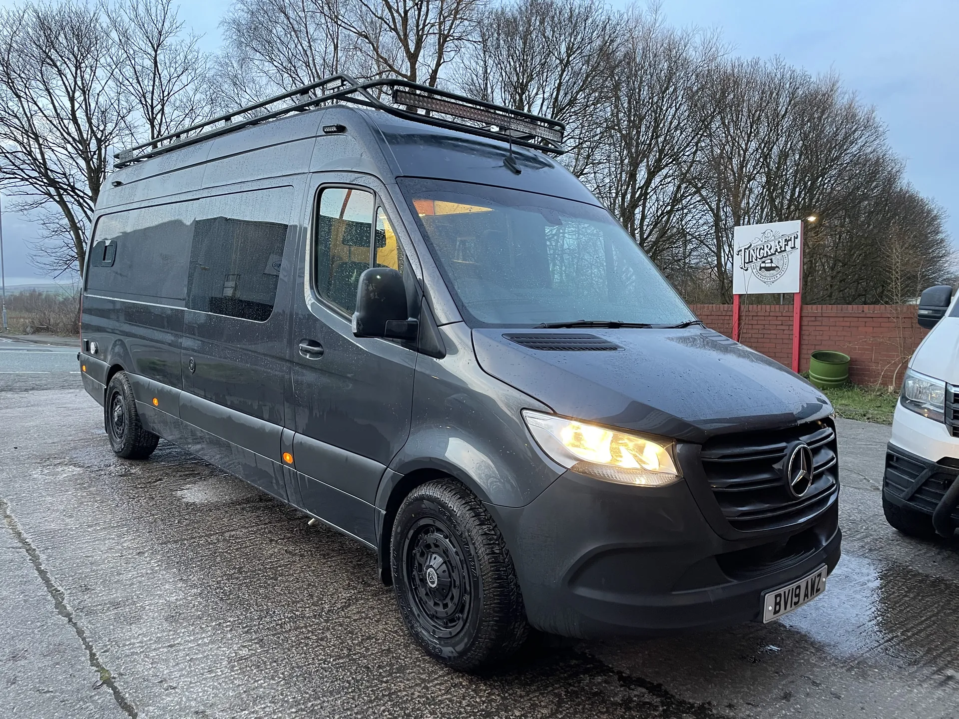 Dark grey Mercedes Sprinter conversion, front three-quarter view with roof rack and black wheels