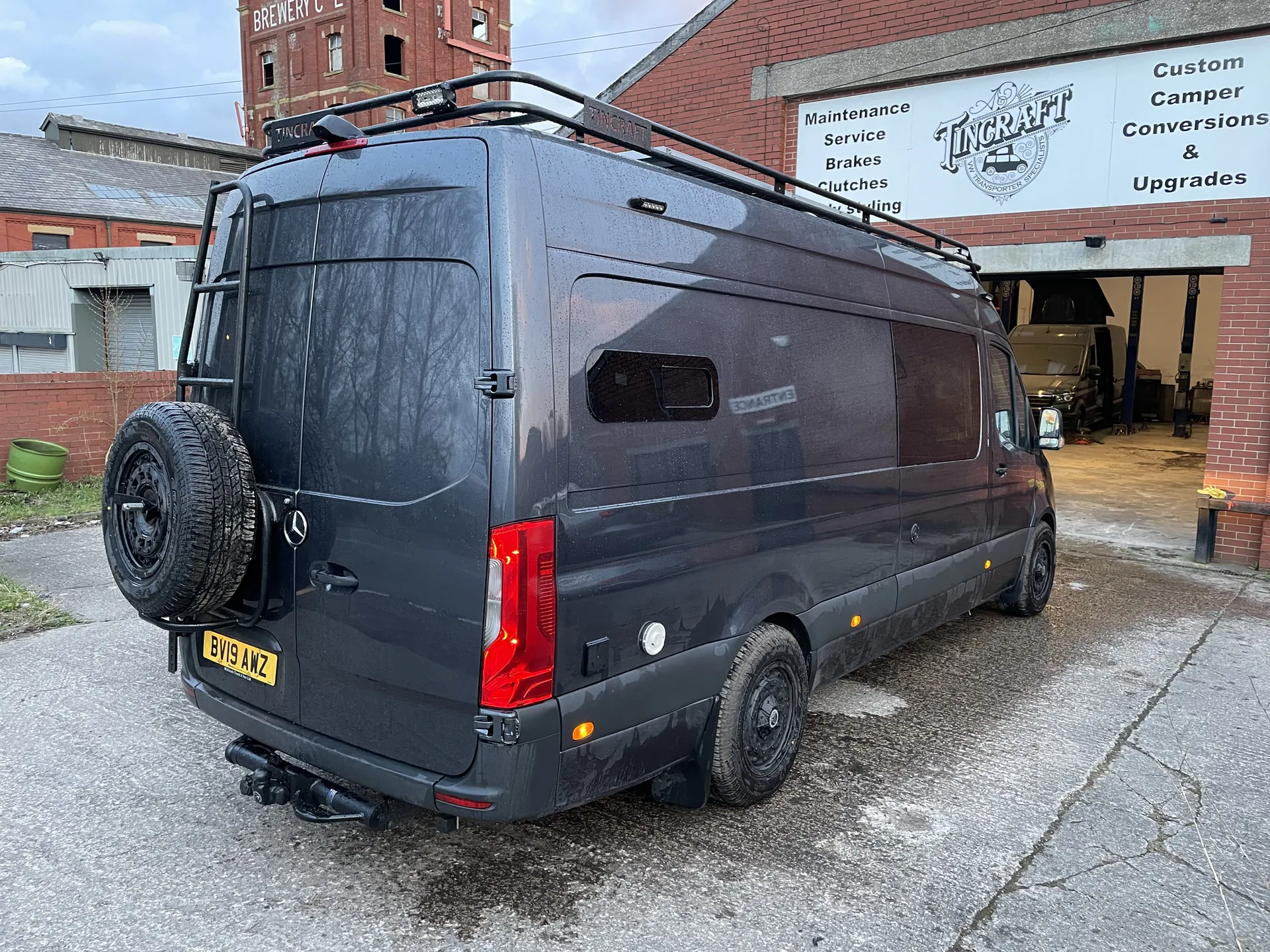 Rear three-quarter view of a grey Sprinter camper with a rear-mounted spare wheel