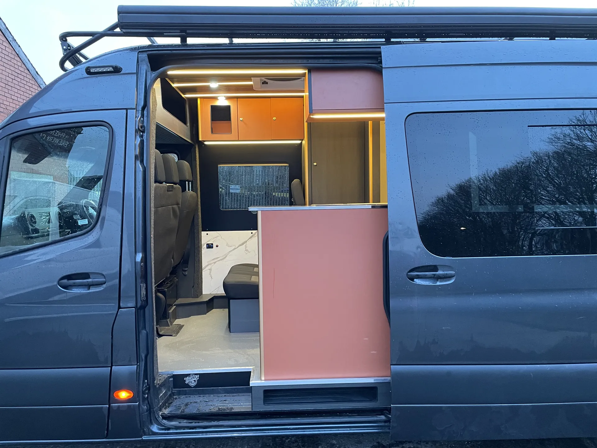 Open side door of a Sprinter camper revealing copper gloss cabinets inside