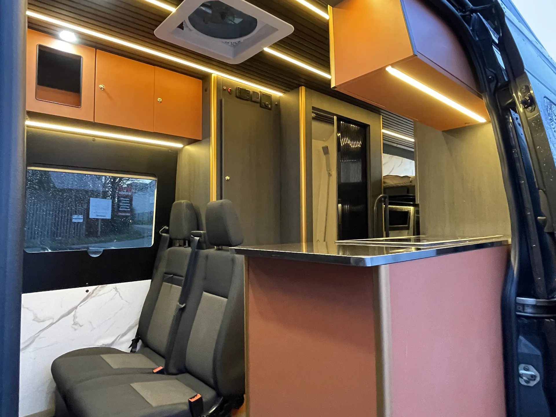 Interior of a Sprinter conversion with copper gloss units, swivel seats and LED cove lighting