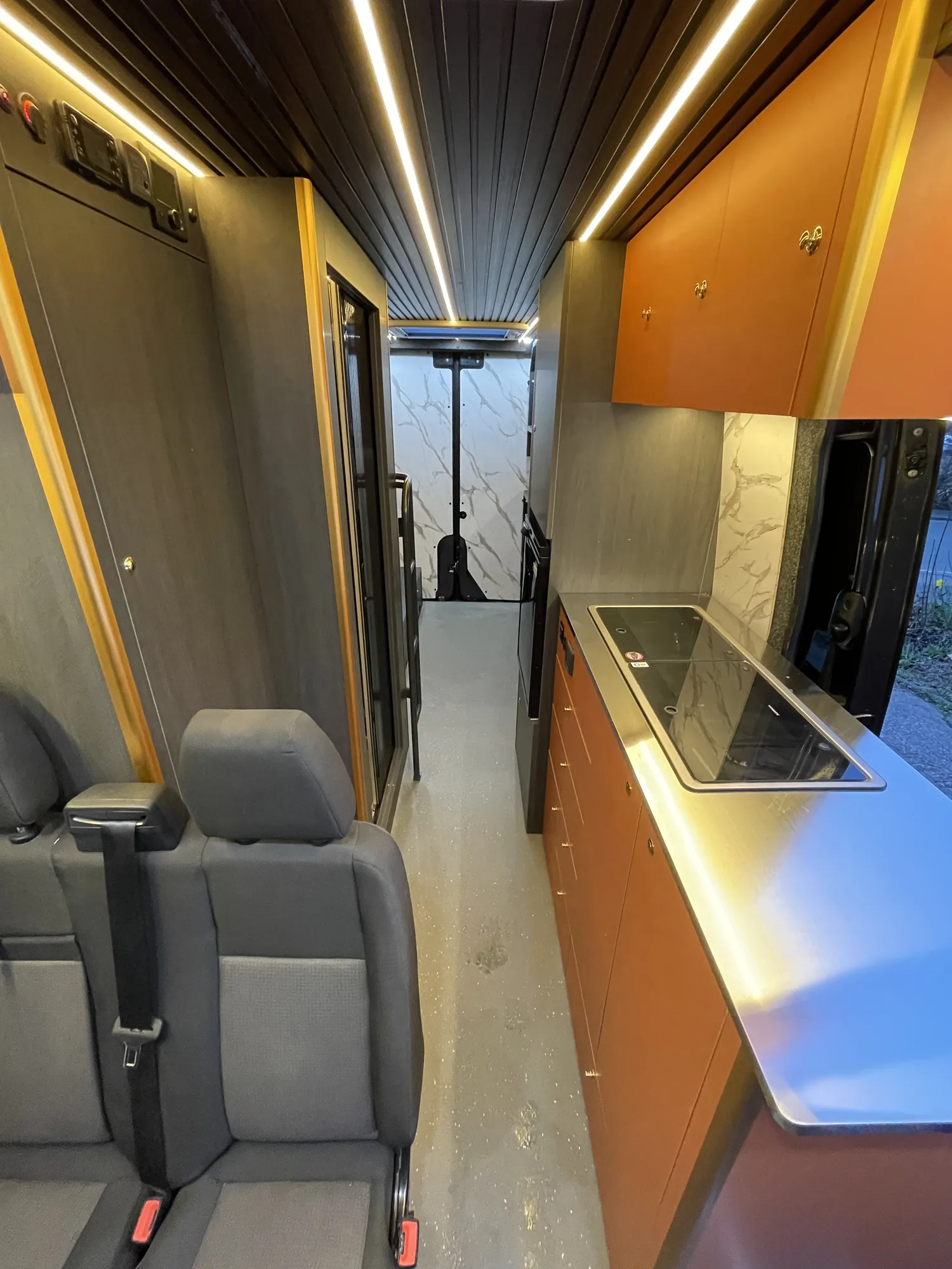 Sprinter camper interior looking toward the galley beneath an oak-slatted ceiling