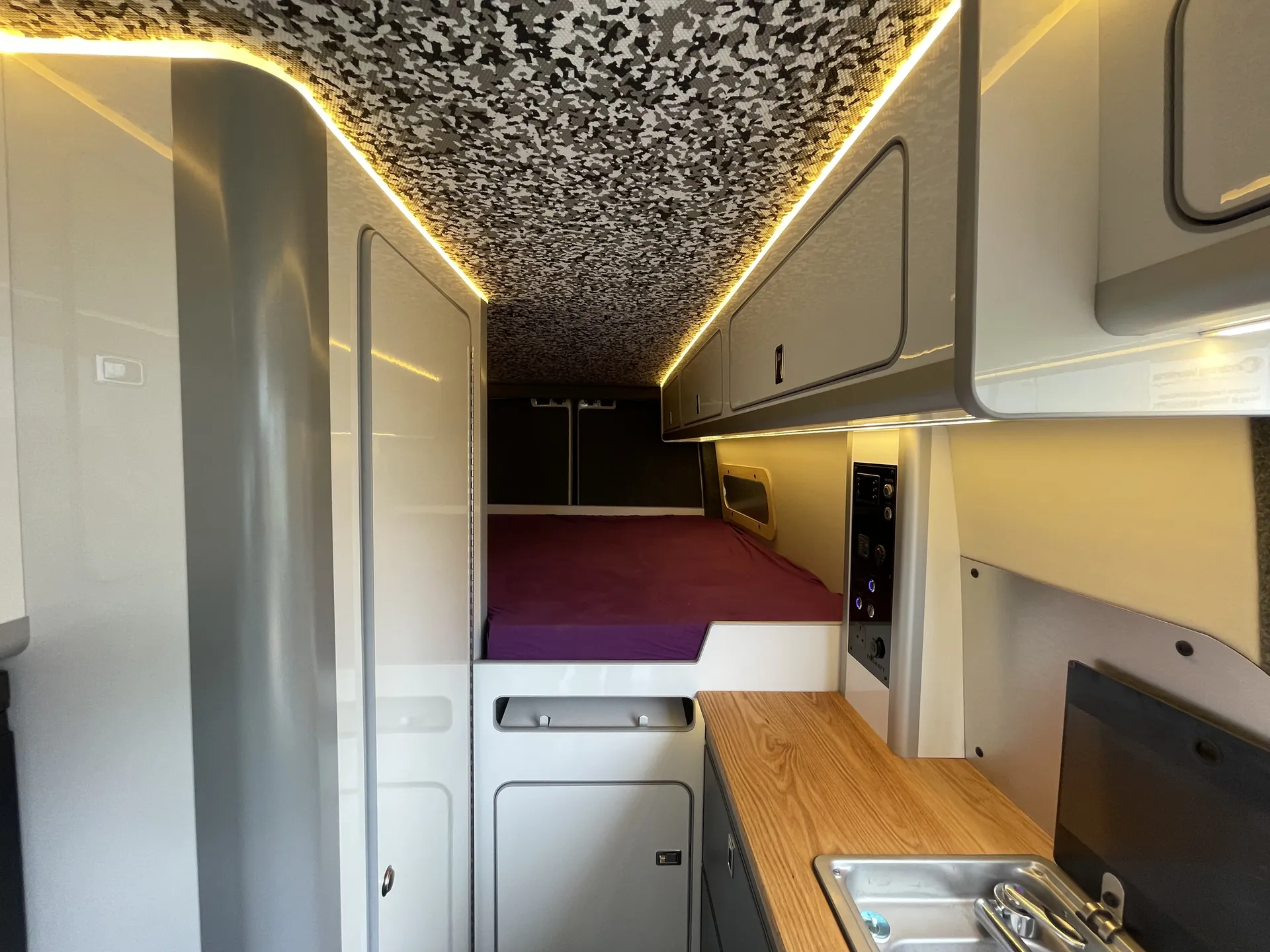 Long interior view of a VW Crafter conversion showing galley, bed and cove lighting