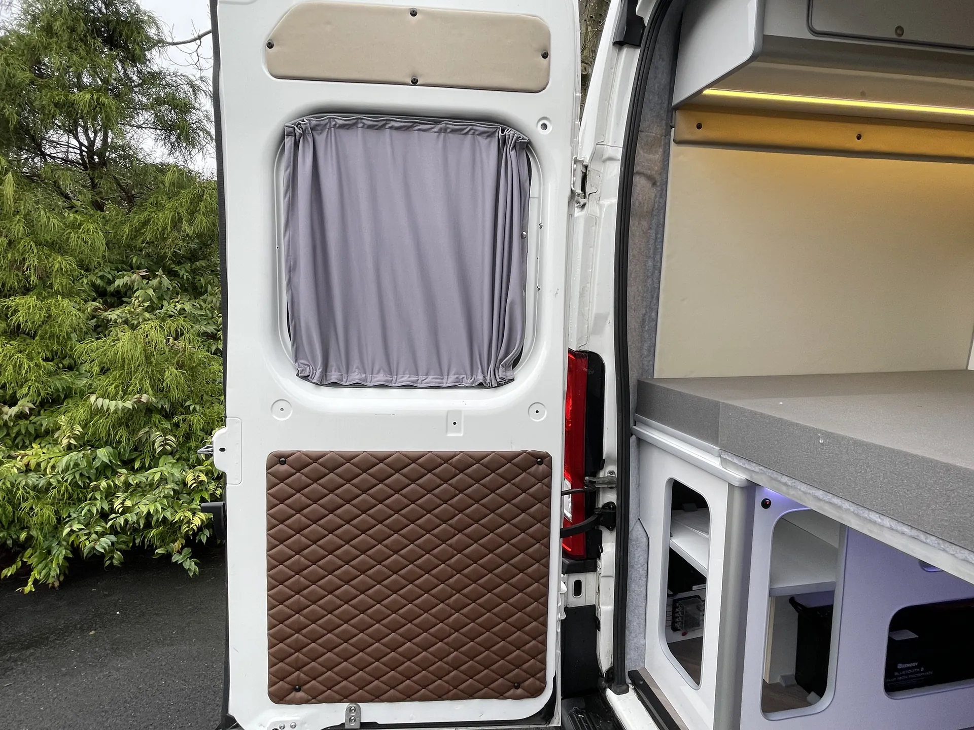 Open side door of a Peugeot Boxer camper showing a brown quilted door panel