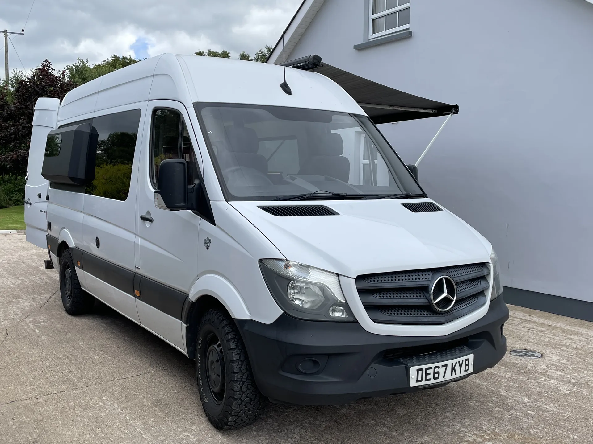 White Mercedes Sprinter camper with the side awning extended, front three-quarter view