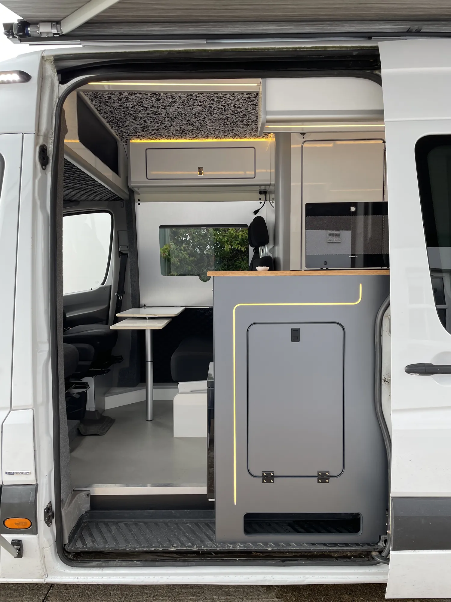 Open side door of a Sprinter camper looking onto the dinette seating