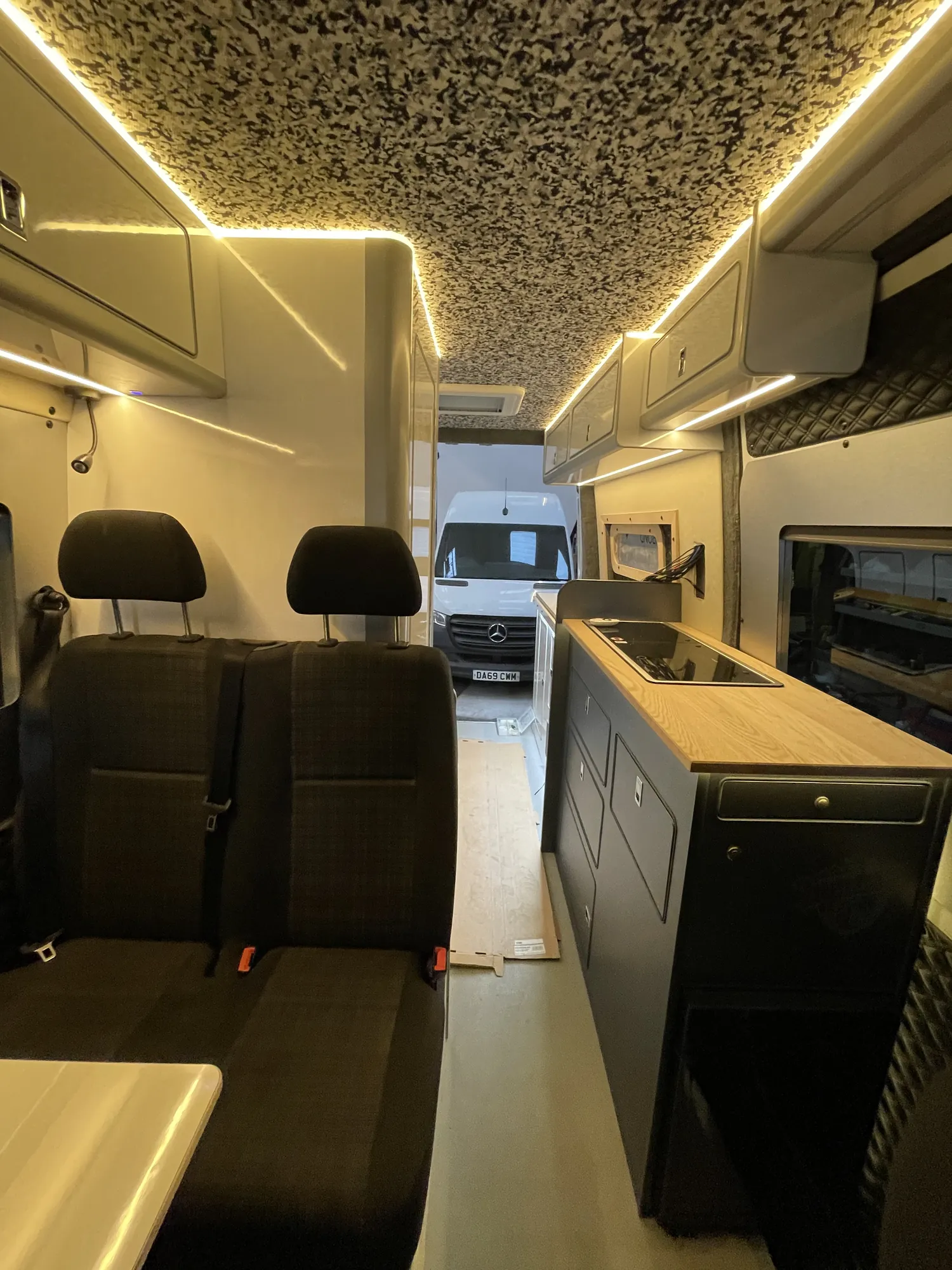 Wide interior of a Mercedes Sprinter conversion showing the seating and galley run