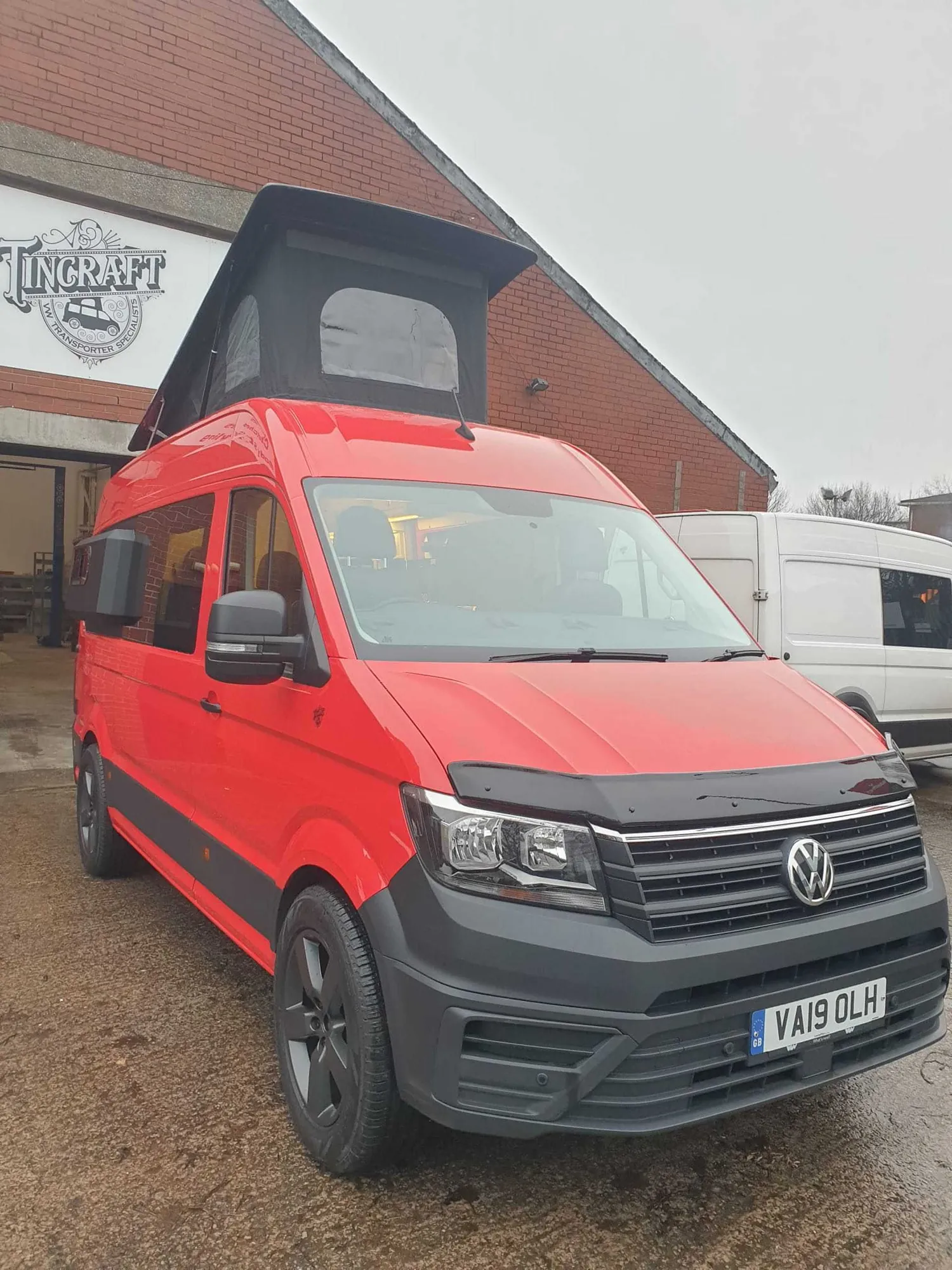 Red VW Crafter campervan with its pop-top roof raised, front three-quarter view